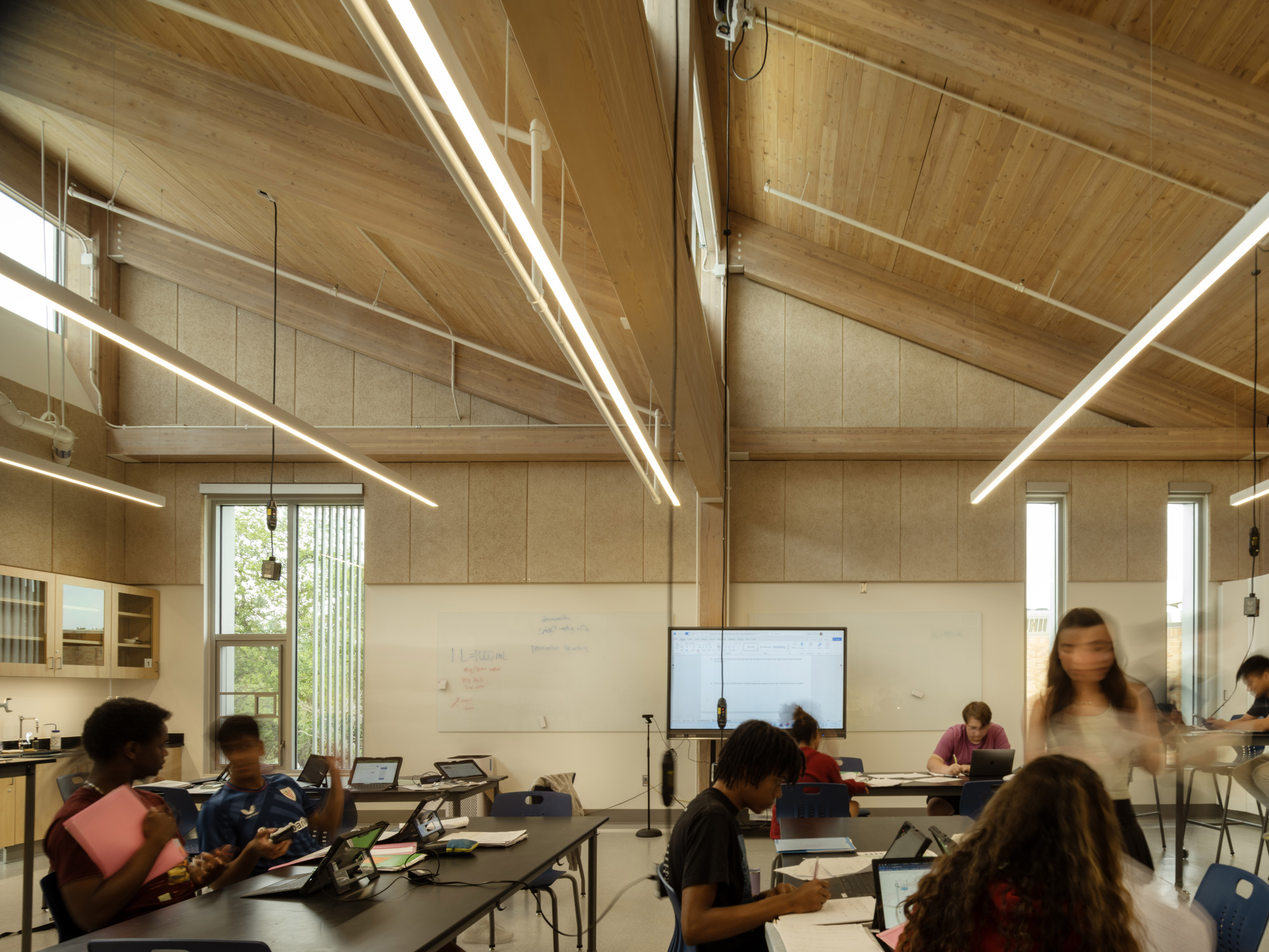 Classroom interior with vaulted timber ceiling, linear pendant lights, and occupants working at tables