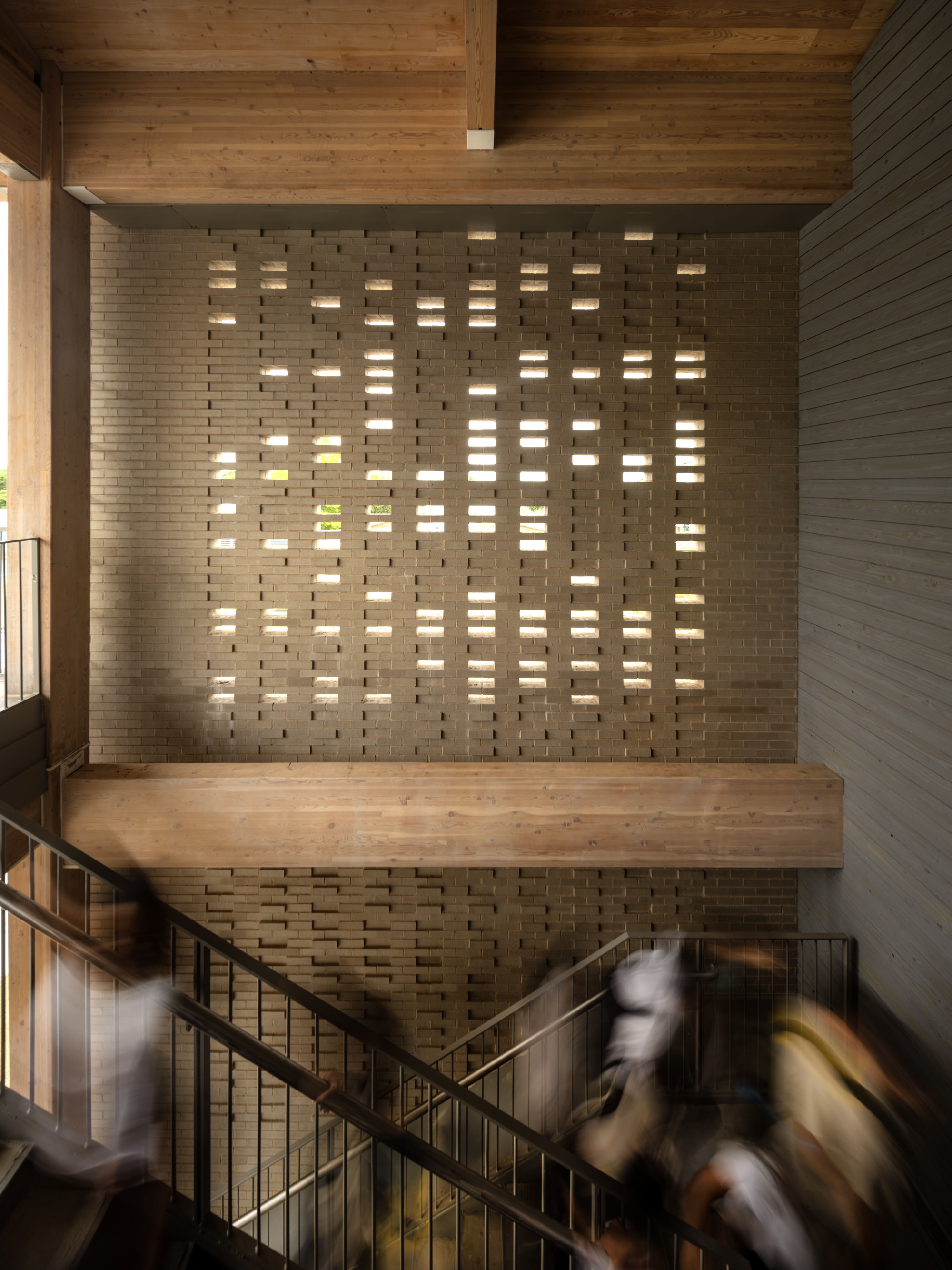 Perforated brick stair wall with light filtering through openings as people descend the steps