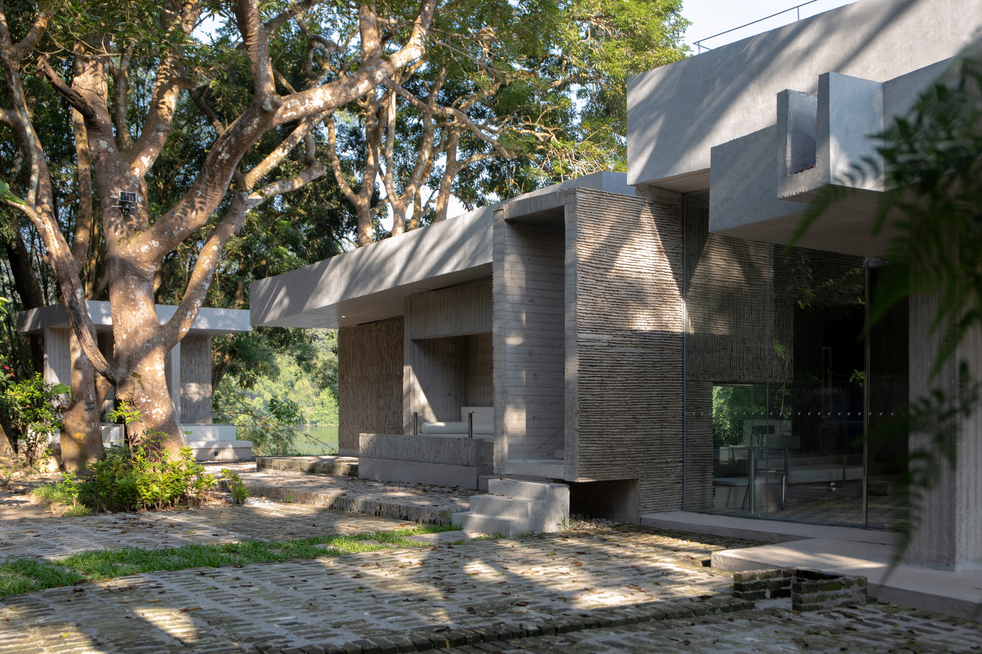 Courtyard with permeable paving, ribbed stone column and dappled morning light filtering through the trees