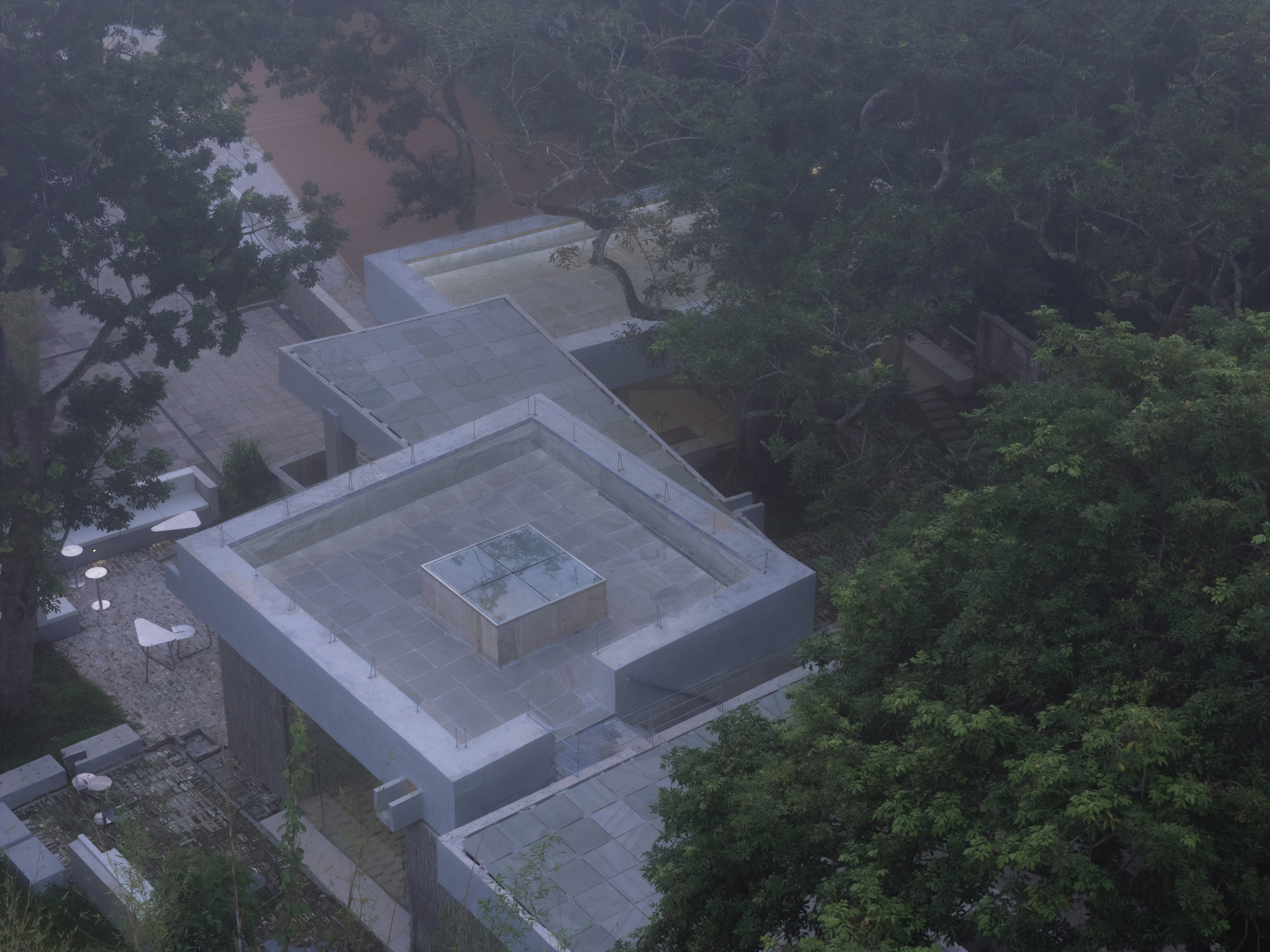 Aerial view of concentric square rooflines with central skylight in forested landscape