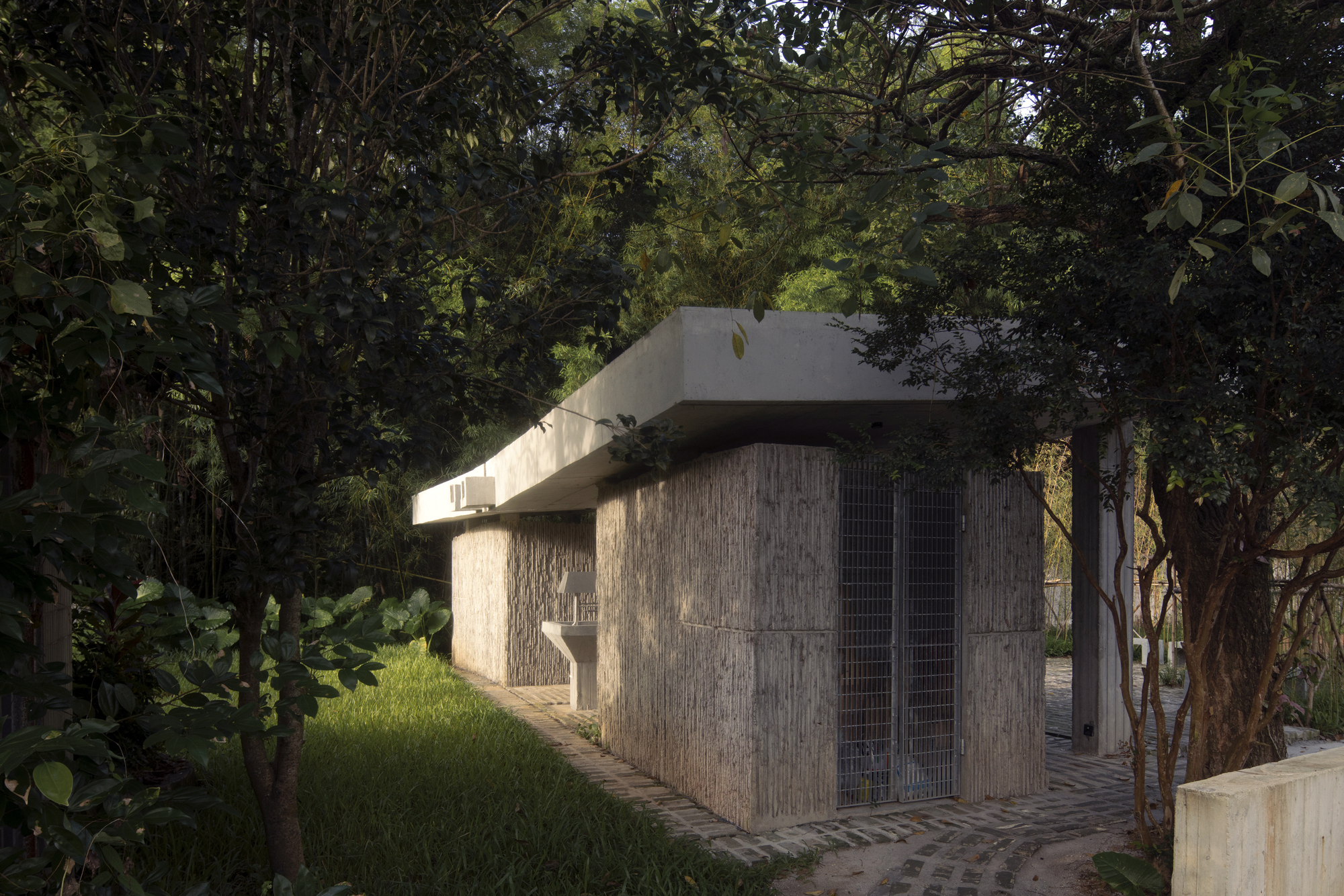 Street view of the board-formed concrete facade with cantilevered roof slab among dense trees