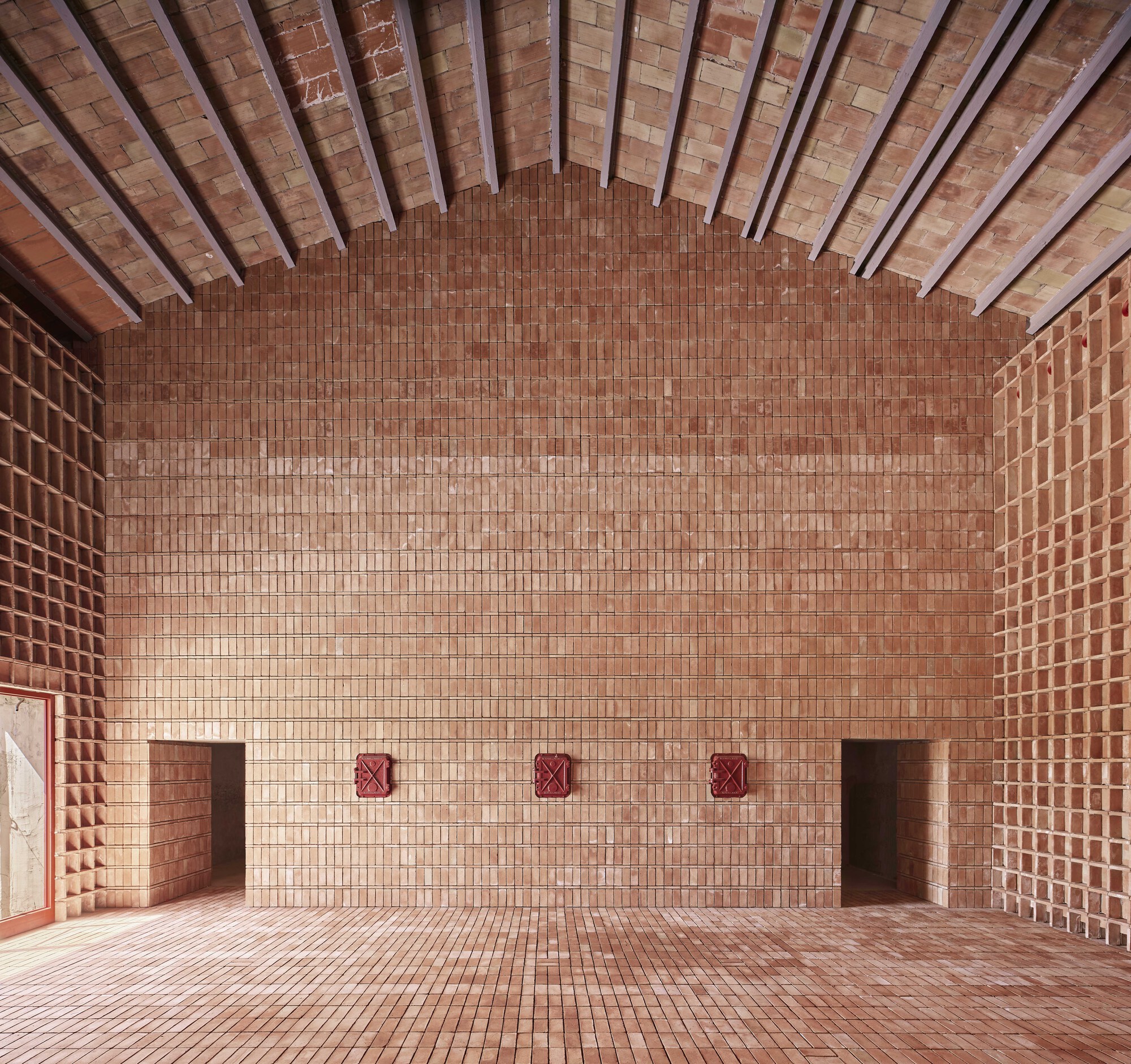 Curved brick wall with three red ventilation grilles below a vaulted tile ceiling with steel beams