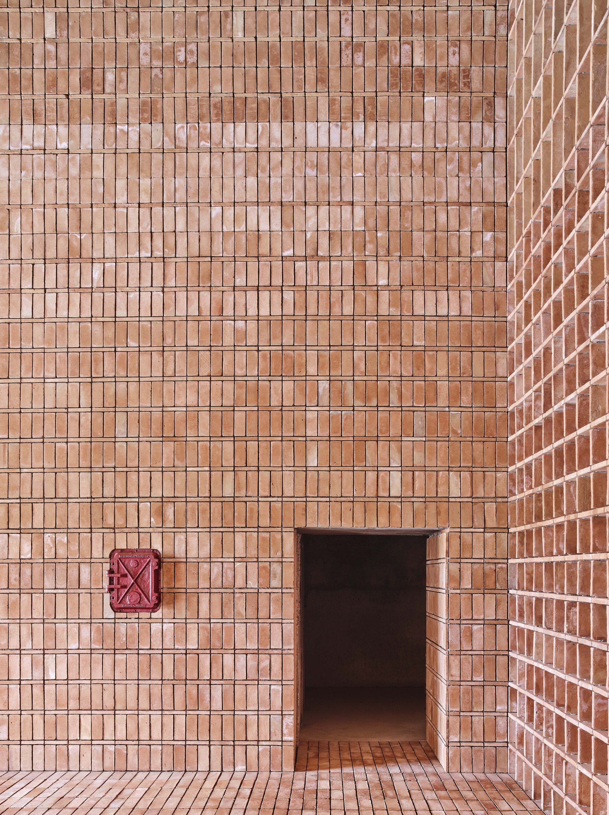 Corner detail of brick wall with a recessed doorway and red metal ventilation grill