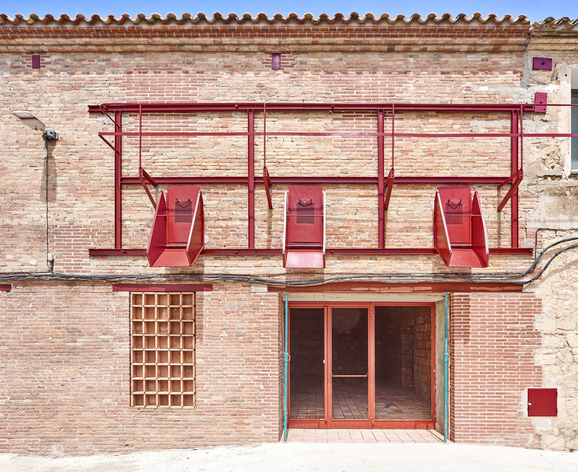 Street facade showing red metal awning structure above glazed entry doors and brick grid window