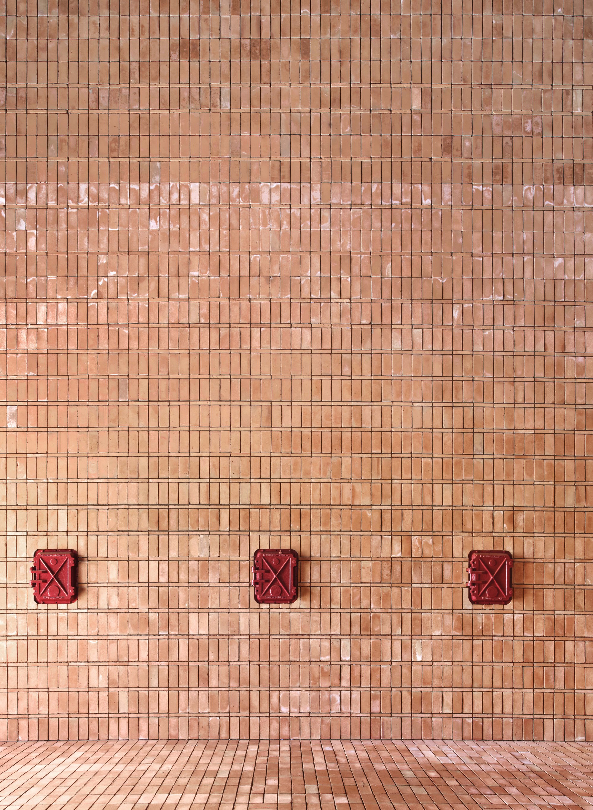 Exterior facade with terracotta mosaic tiles and three red decorative metal panels near the paved ground
