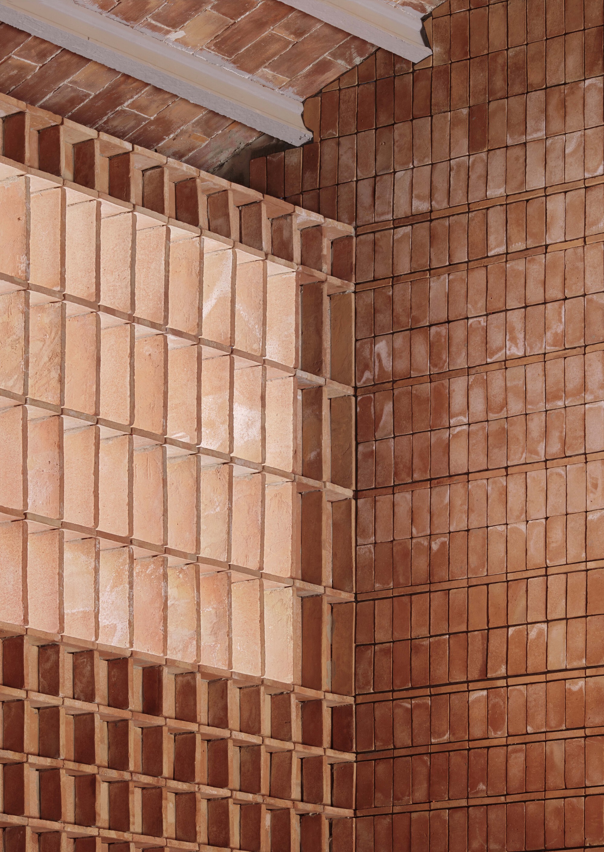 Close-up of terracotta brick corner showing alternating projecting courses and varied tile orientations under a timber ceiling