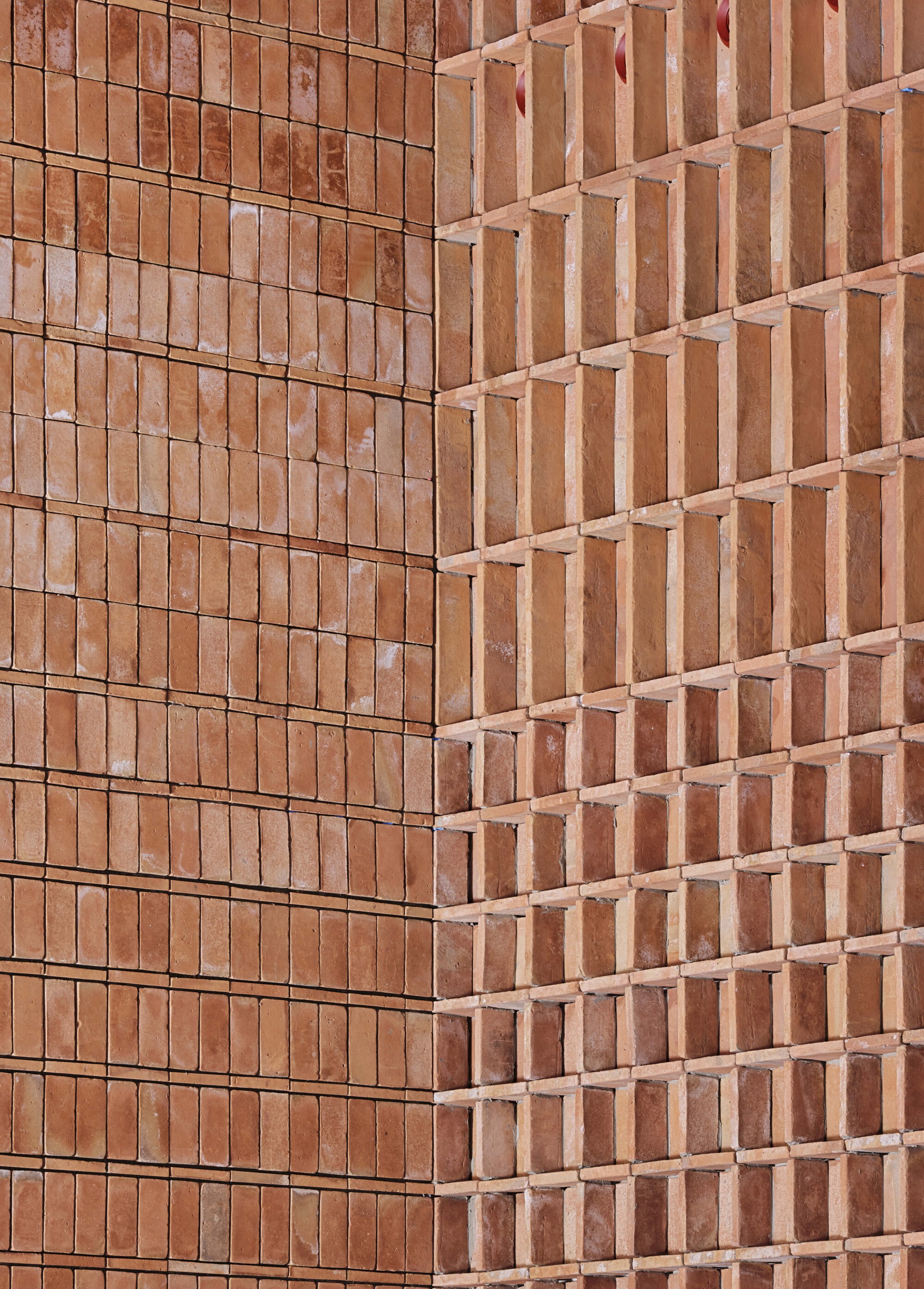 Corner detail of two terracotta brick facades meeting at differing textures and relief patterns