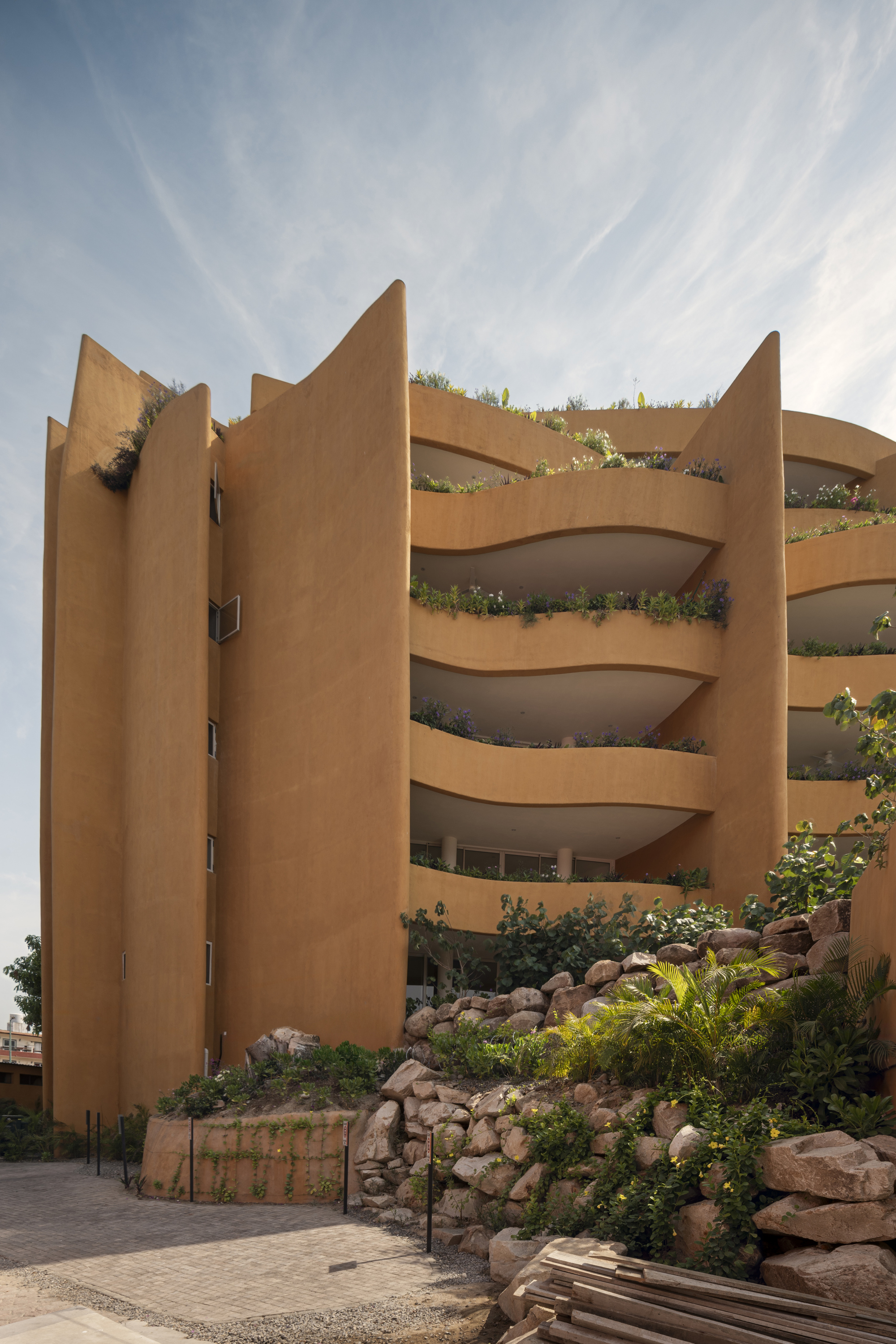 Curved balconies with planted beds cascading down the facade behind a rock garden at street level