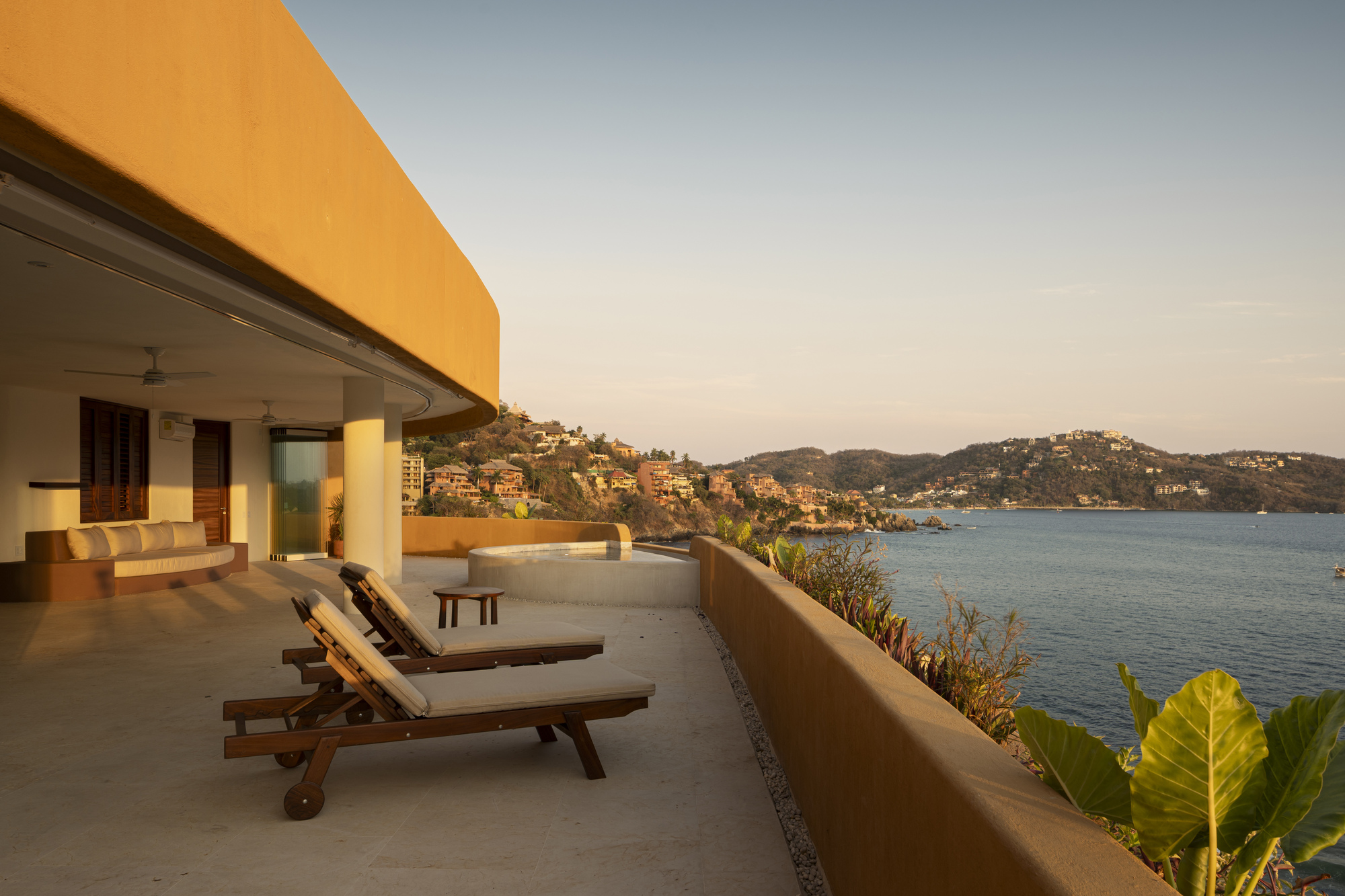 Terrace with teak loungers and tropical plants framing the bay view under a golden evening sky