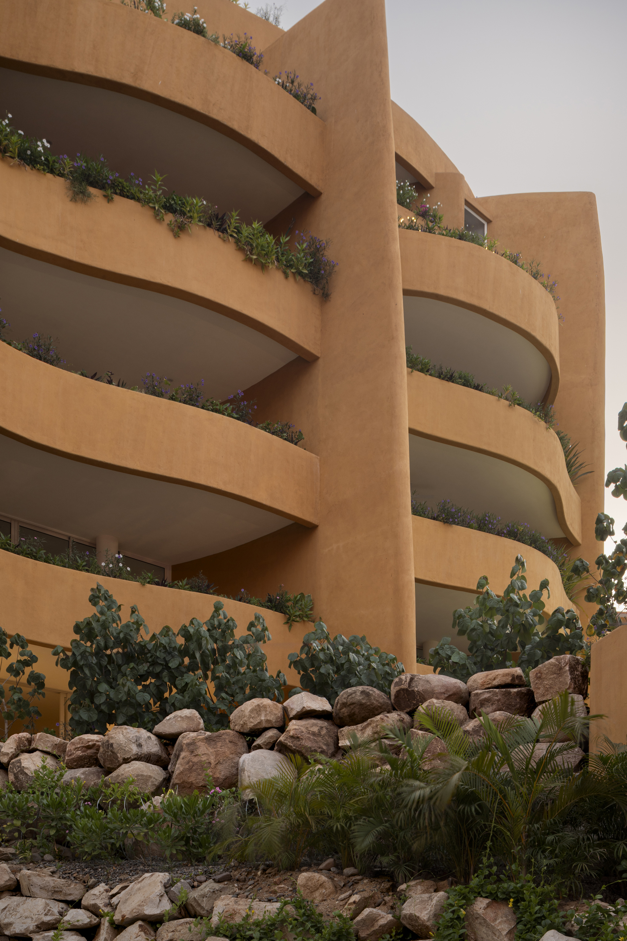 Curved balconies with planted edges rise above a terraced rock garden with cacti and ferns