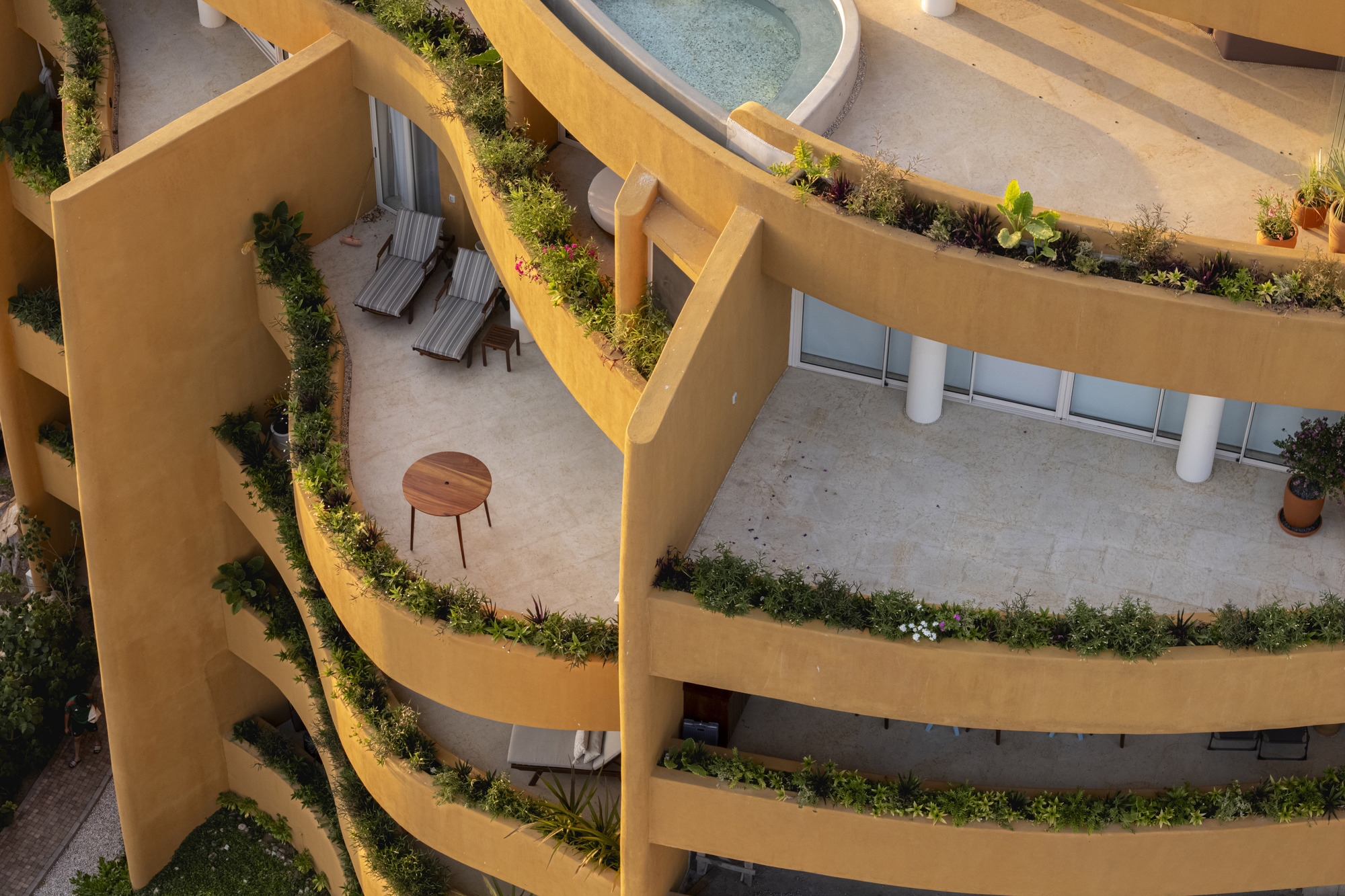 Top-down view of planted terraces wrapping around curved balconies with outdoor furniture and a pool