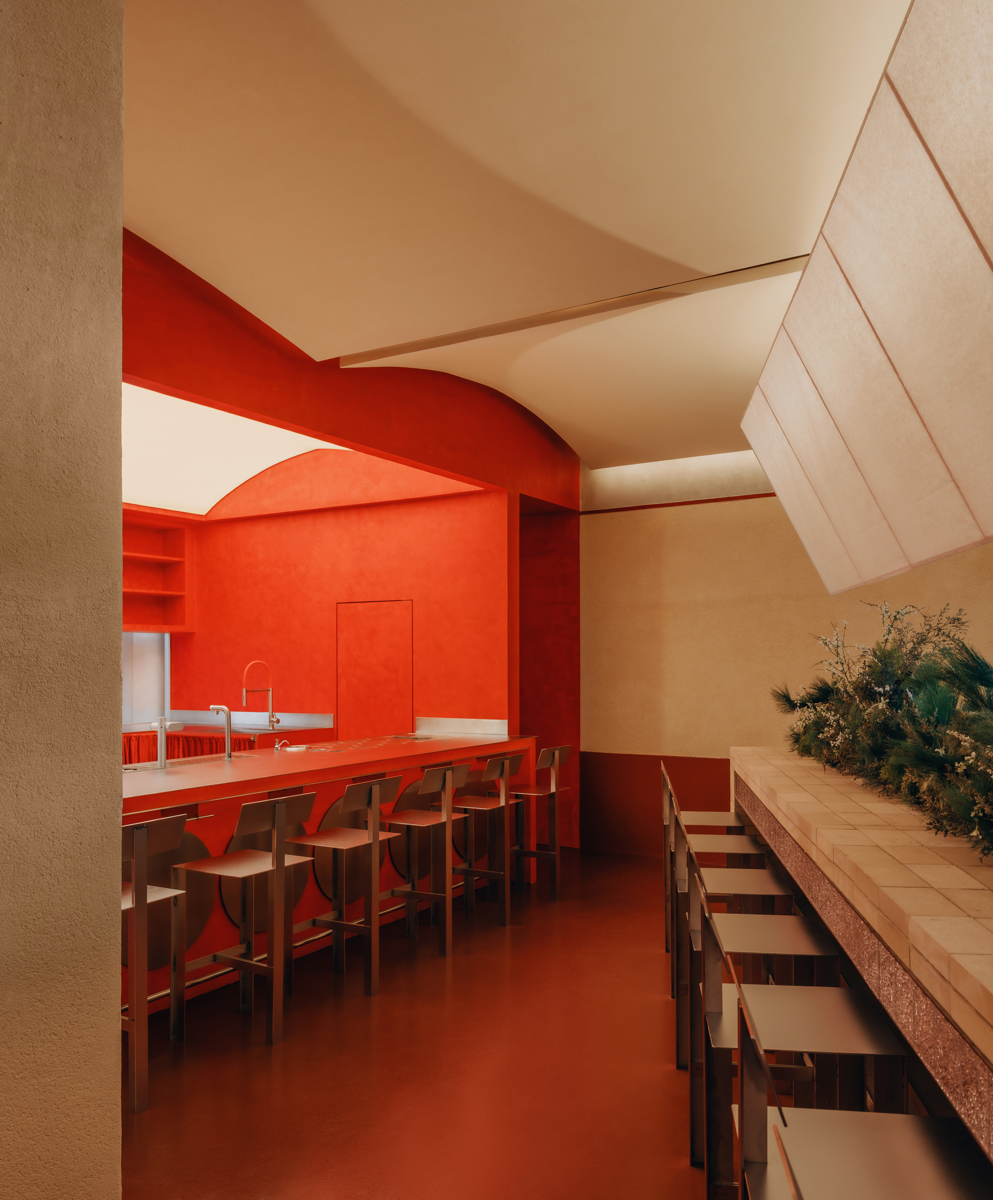 Interior dining space with red bar counter and arched opening beneath a sloped plywood ceiling