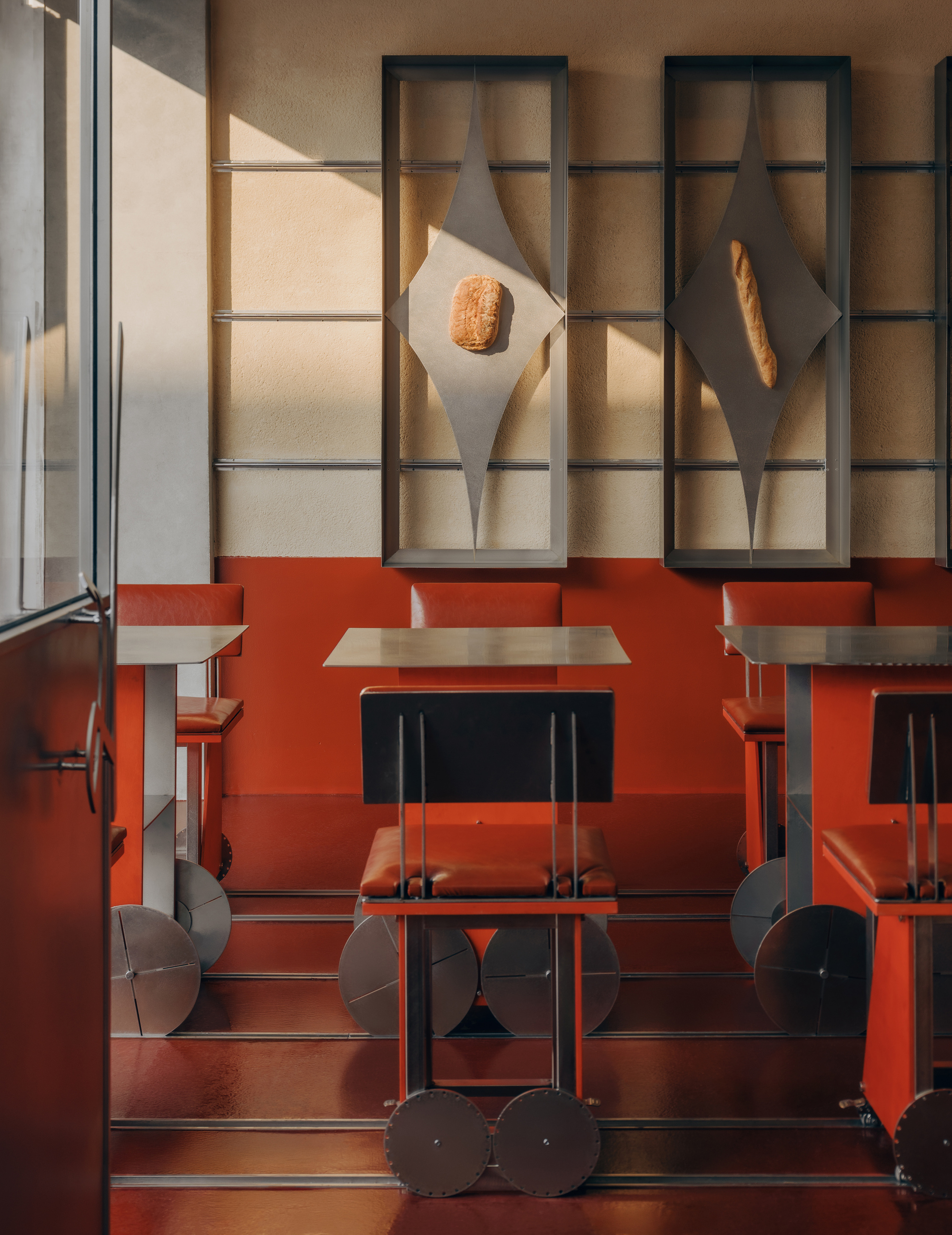 Dining booth with red banquette beneath backlit display niches holding bread loaves in afternoon sun