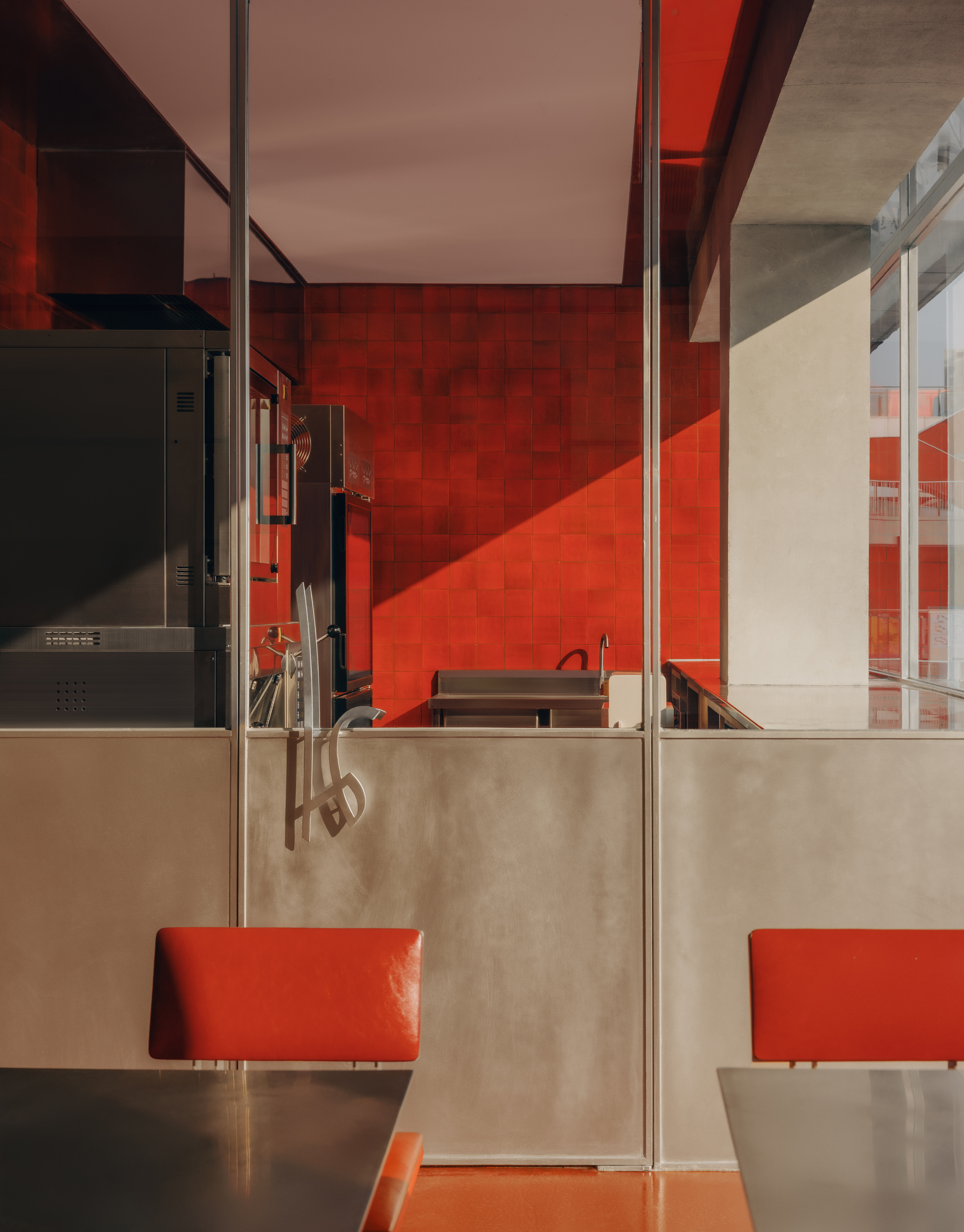 Dining area with red tile walls, stainless steel partitions, and orange banquettes beneath skylights