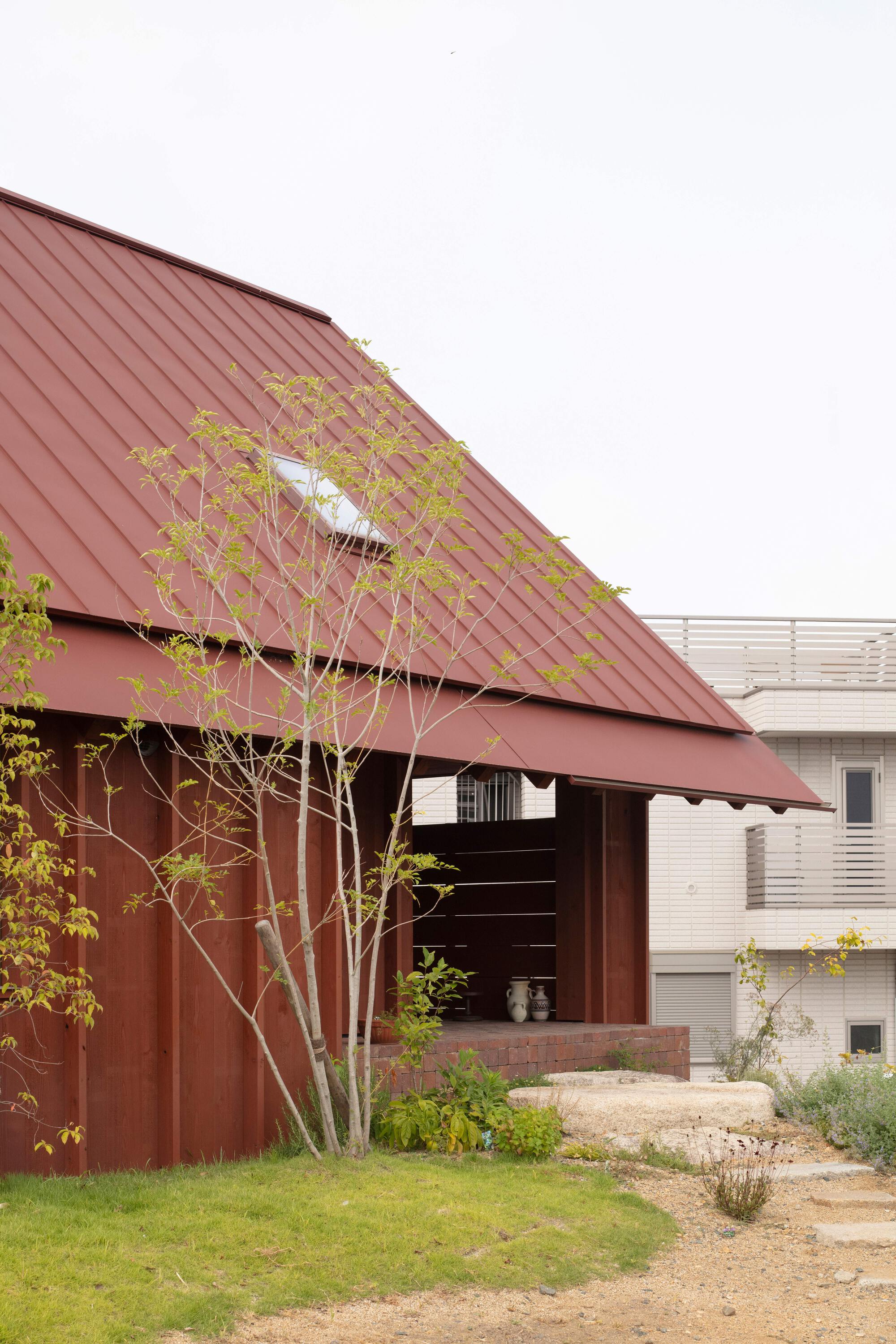 Covered entry with sloped metal roof partially screened by a young planted tree