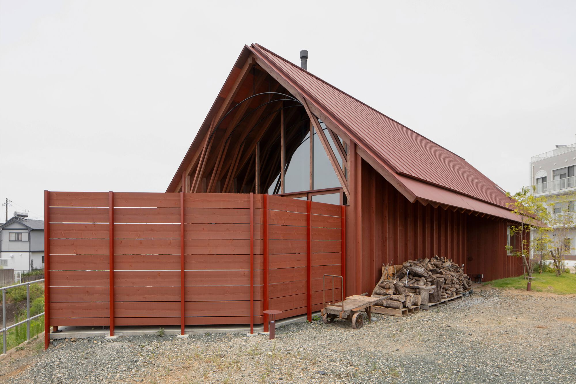 Gabled volume with ribbed metal roof and timber cladding beside a gravel drive