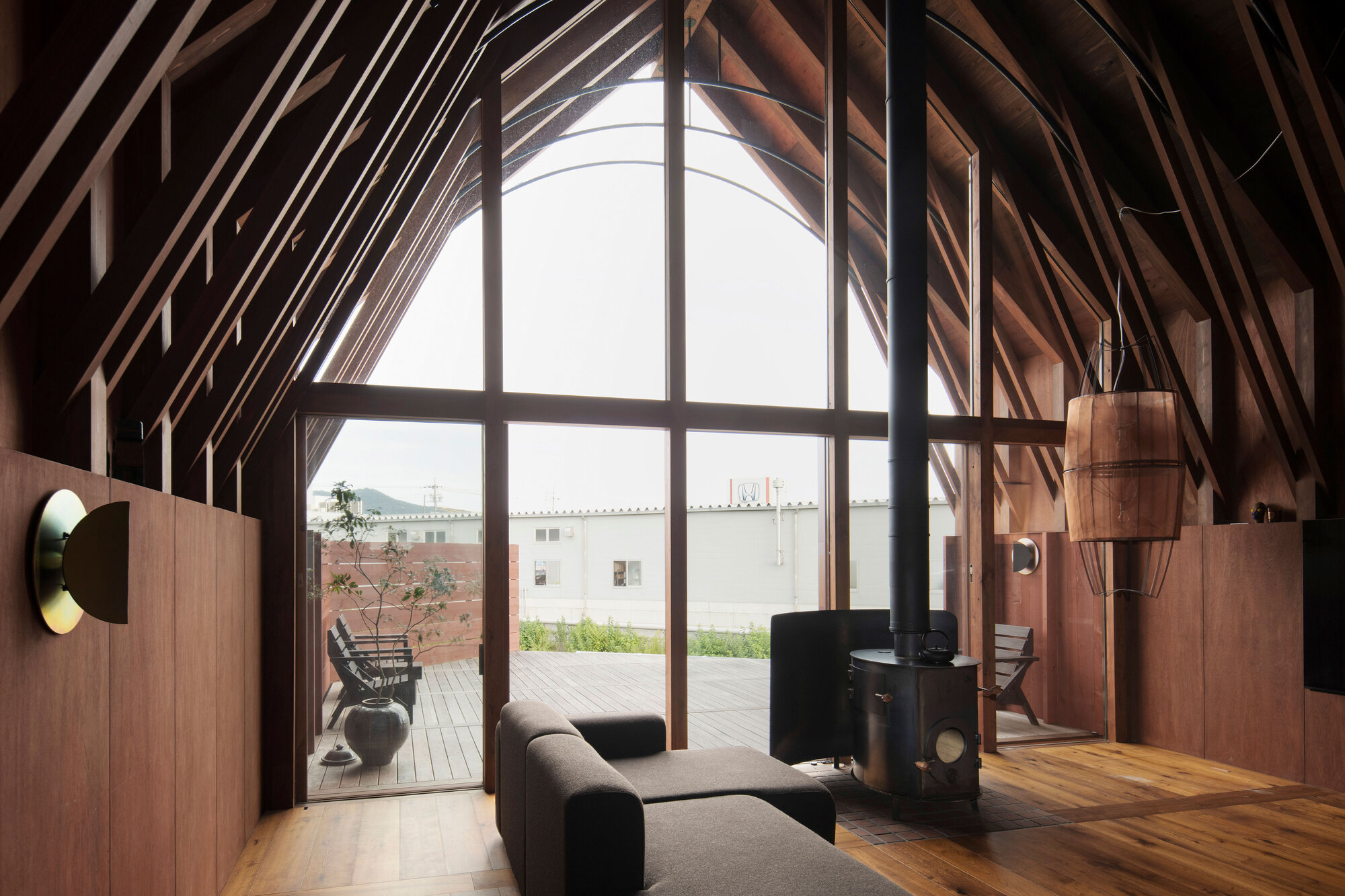 Interior living space with exposed timber rib structure framing a glazed gable end overlooking an adjacent building