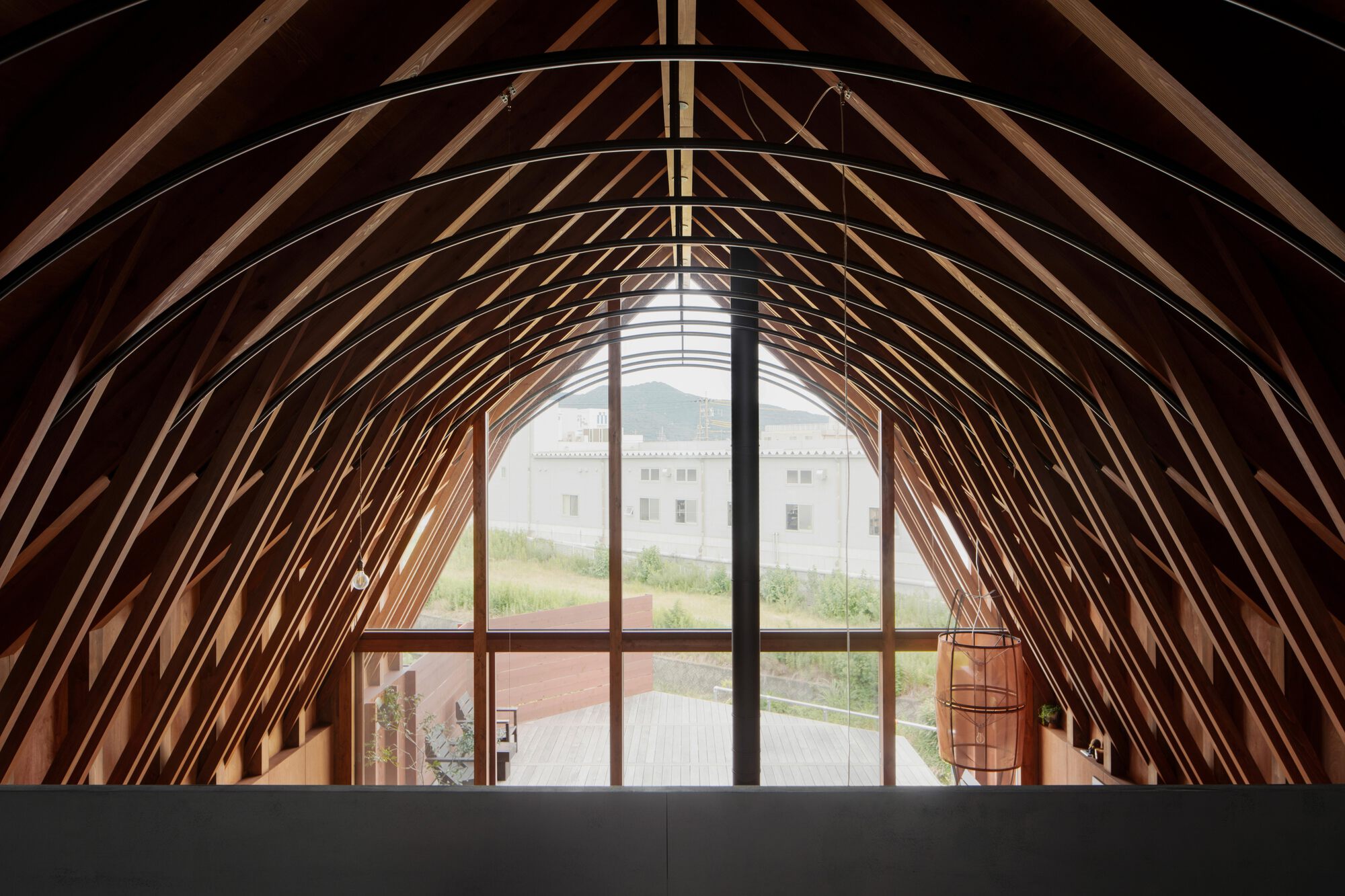 Arched timber rib ceiling framing tall glazed opening with view to courtyard and neighboring structure