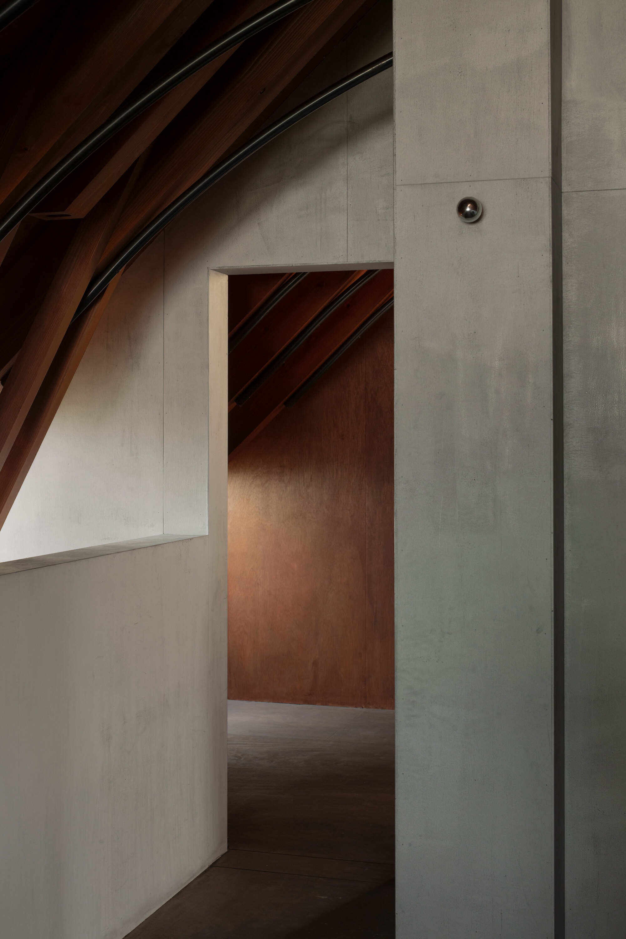 Doorway opening in white wall leading to timber-lined corridor under diagonal roof rafters