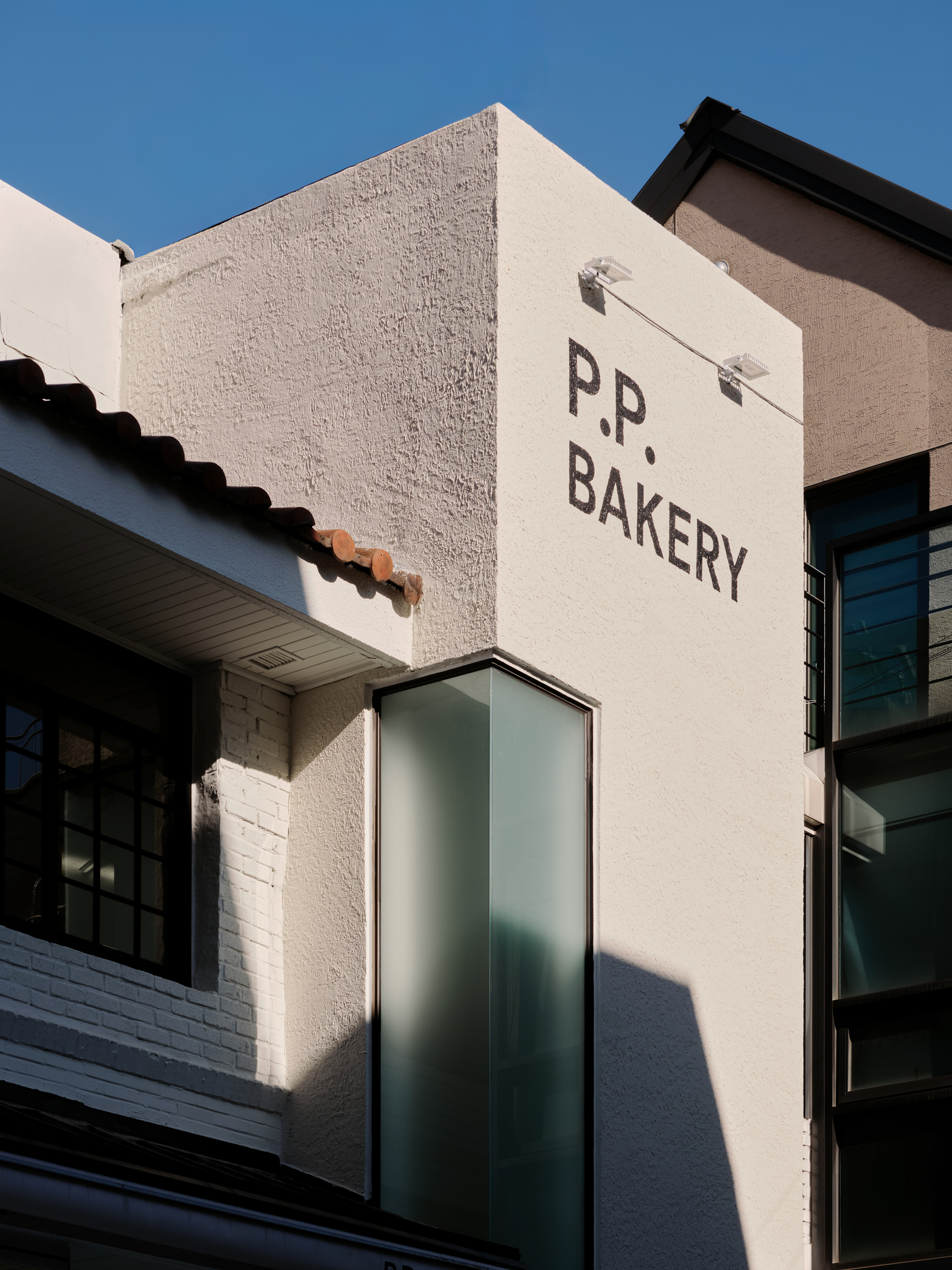 Painted P.P. BAKERY logo on a stucco wall above the tiled eaves of the original house