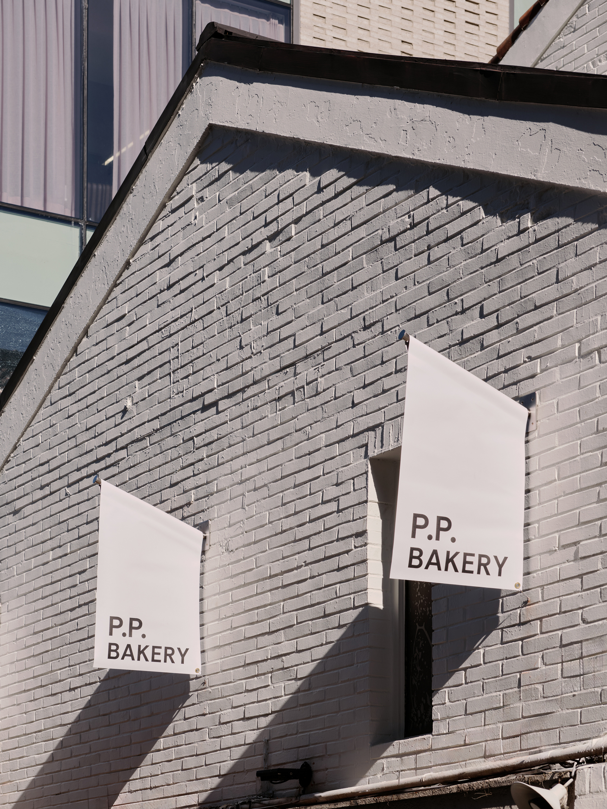 Two cloth banners reading P.P. BAKERY hung against a grey-painted brick gable