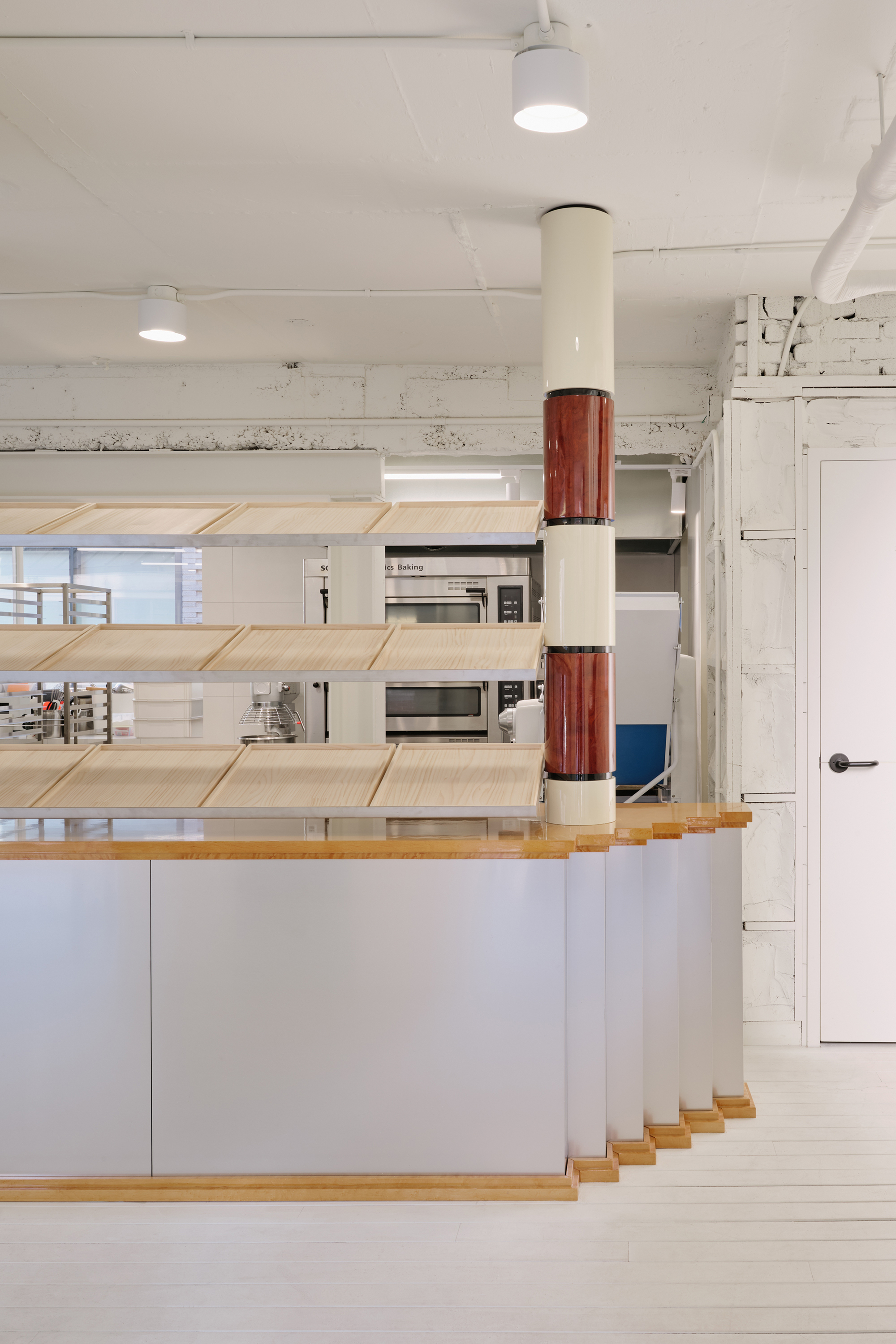 Ground-floor counter with timber shelves wrapped around a steel column with a maroon sleeve
