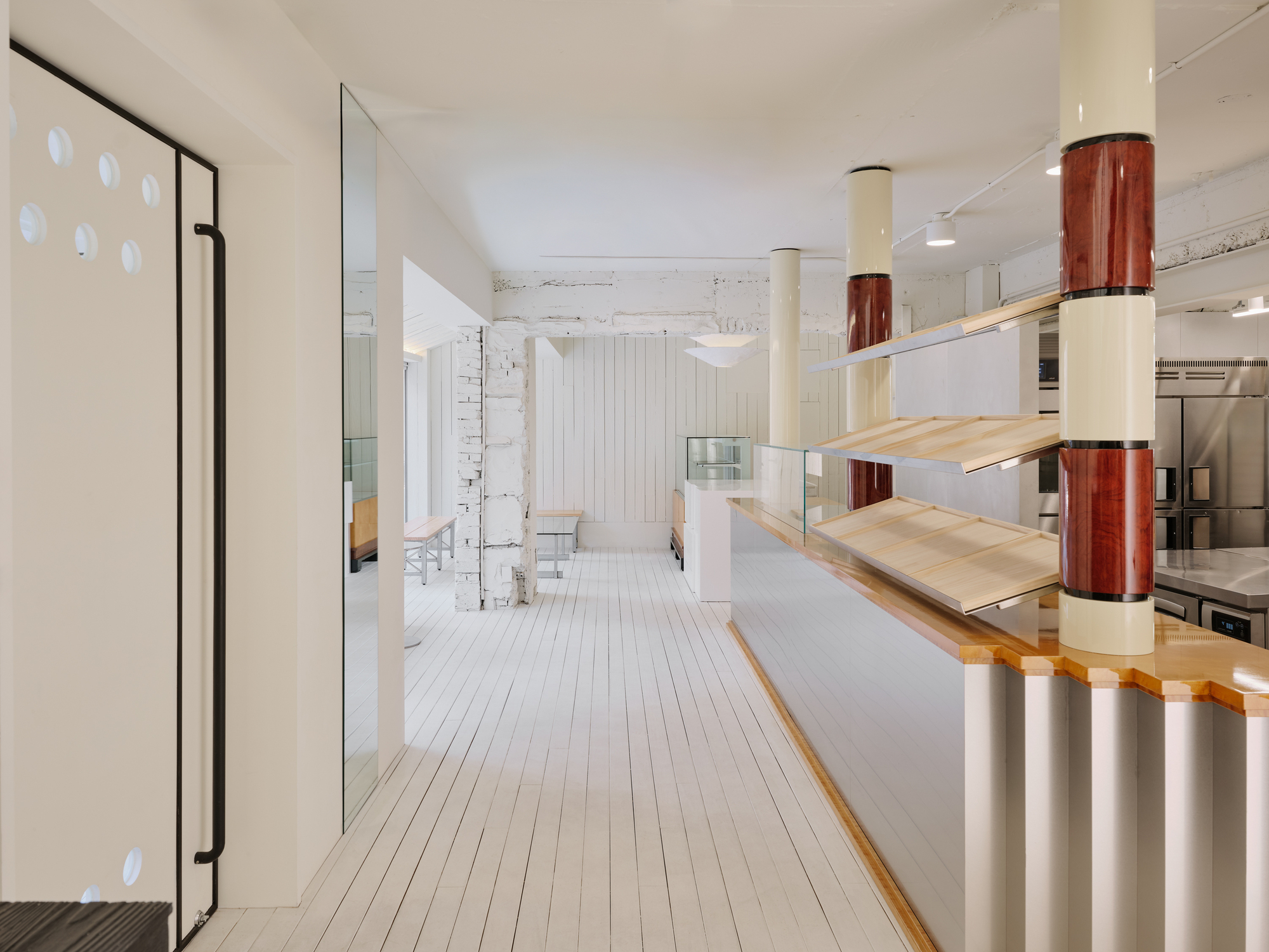 Long view of the ground floor showing the bakery counter, maroon-sleeved columns and the rough white-painted brickwork