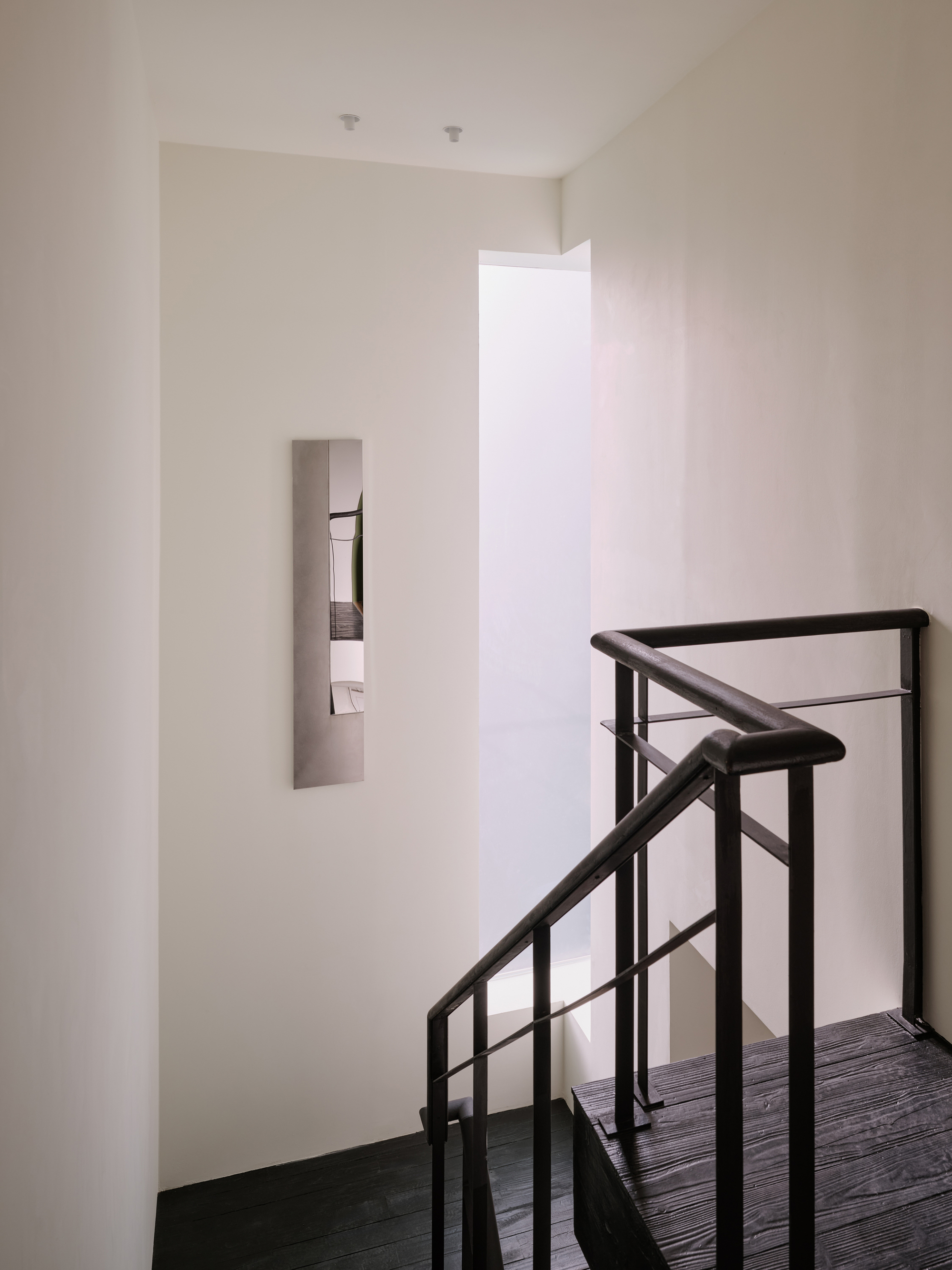 Quiet upper-floor stair landing with a small mirrored panel on the white wall