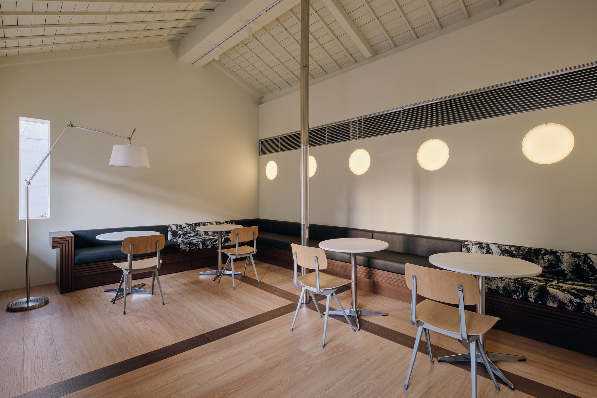 Cafe seating with round tables and a row of glowing circular wall lights