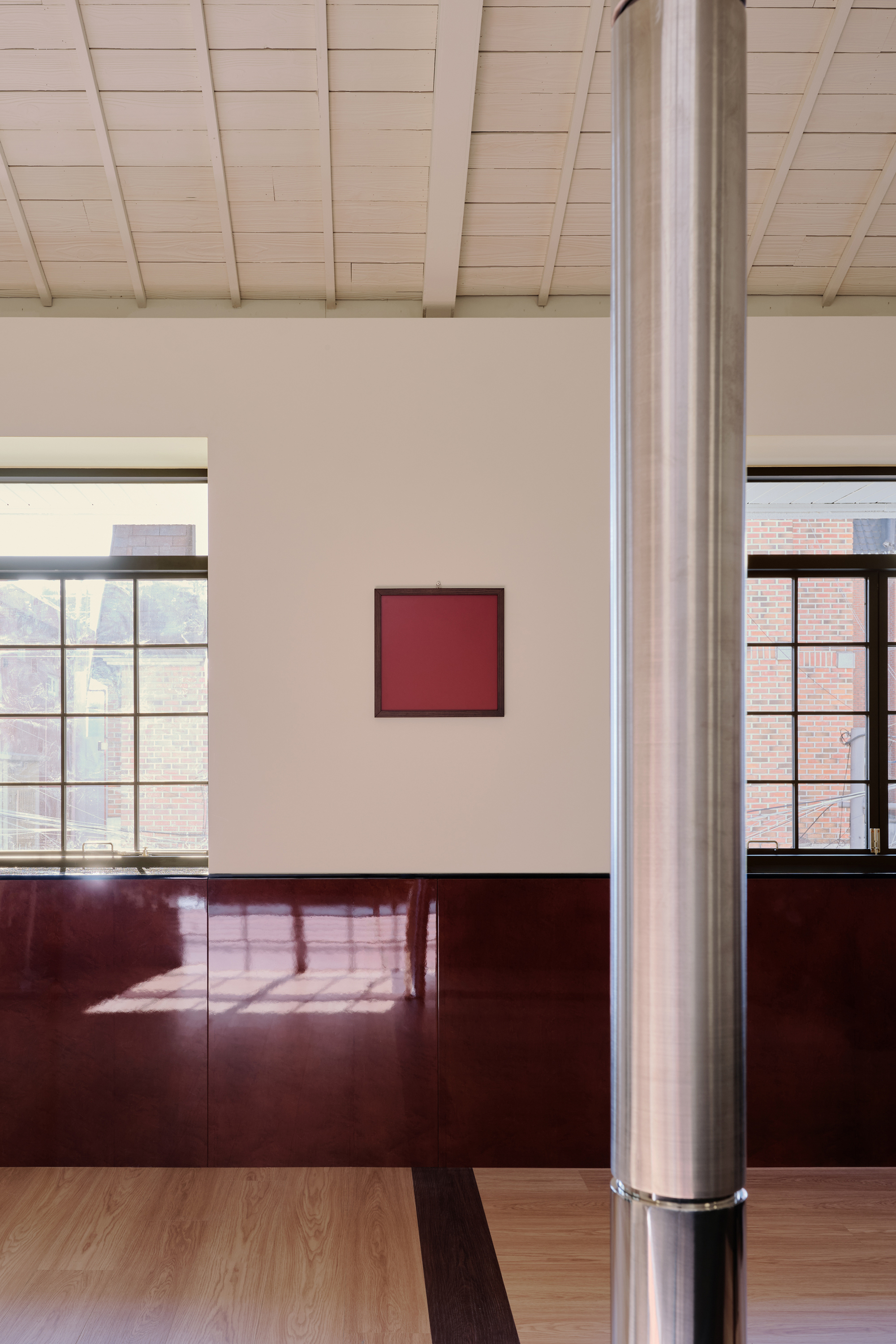 Upper-floor corner with two punched windows, a small red painting and a glossy maroon dado