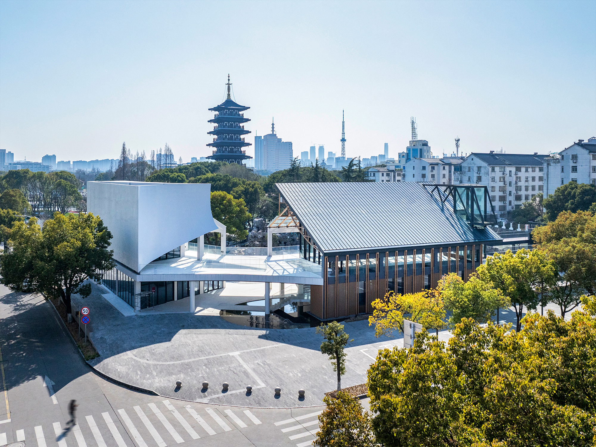 Aerial view of two volumes with sloped metal roofs facing a plaza with pedestrian crossings