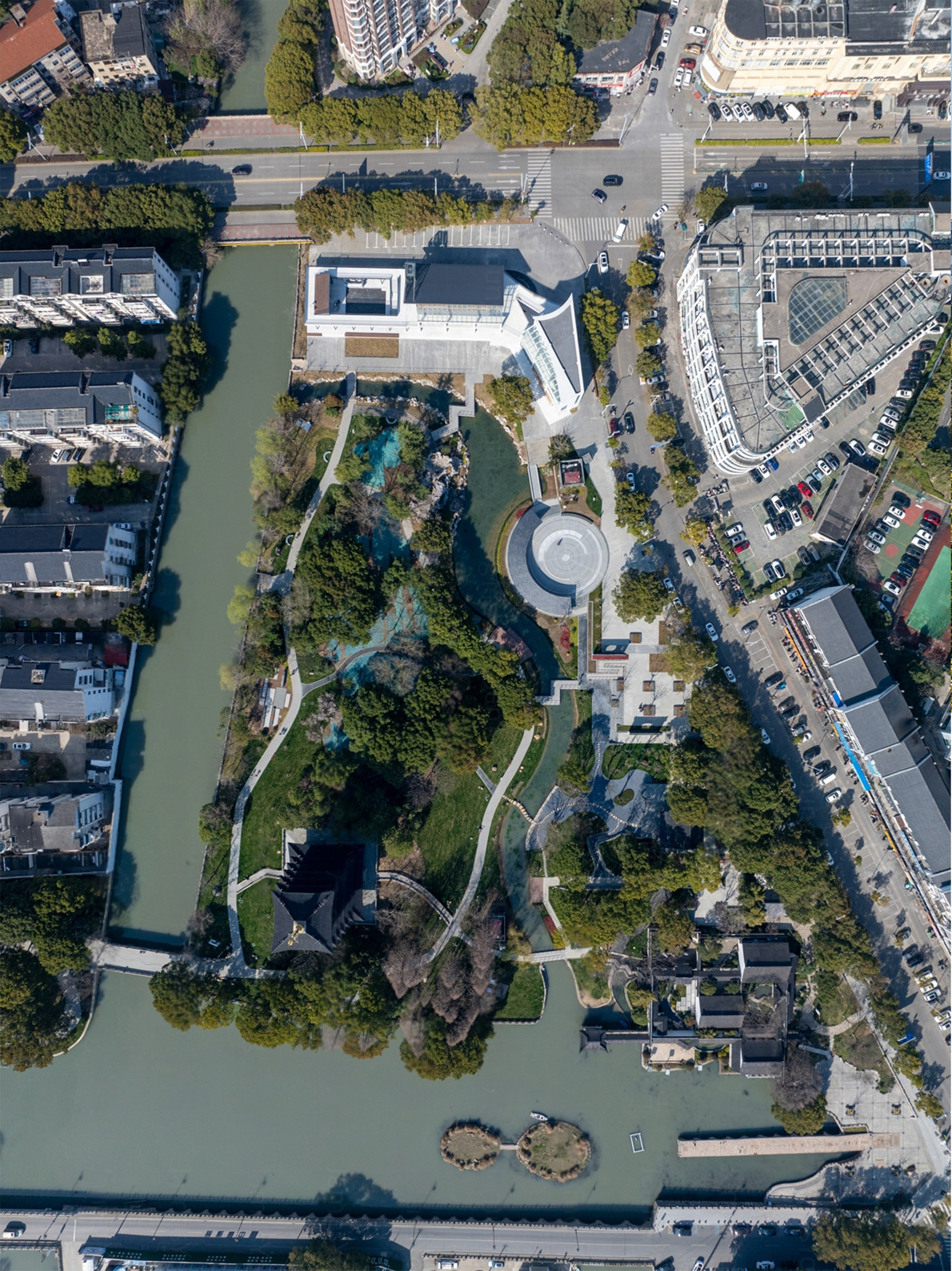 Drone view of white buildings and circular pavilion surrounded by winding pathways and waterways