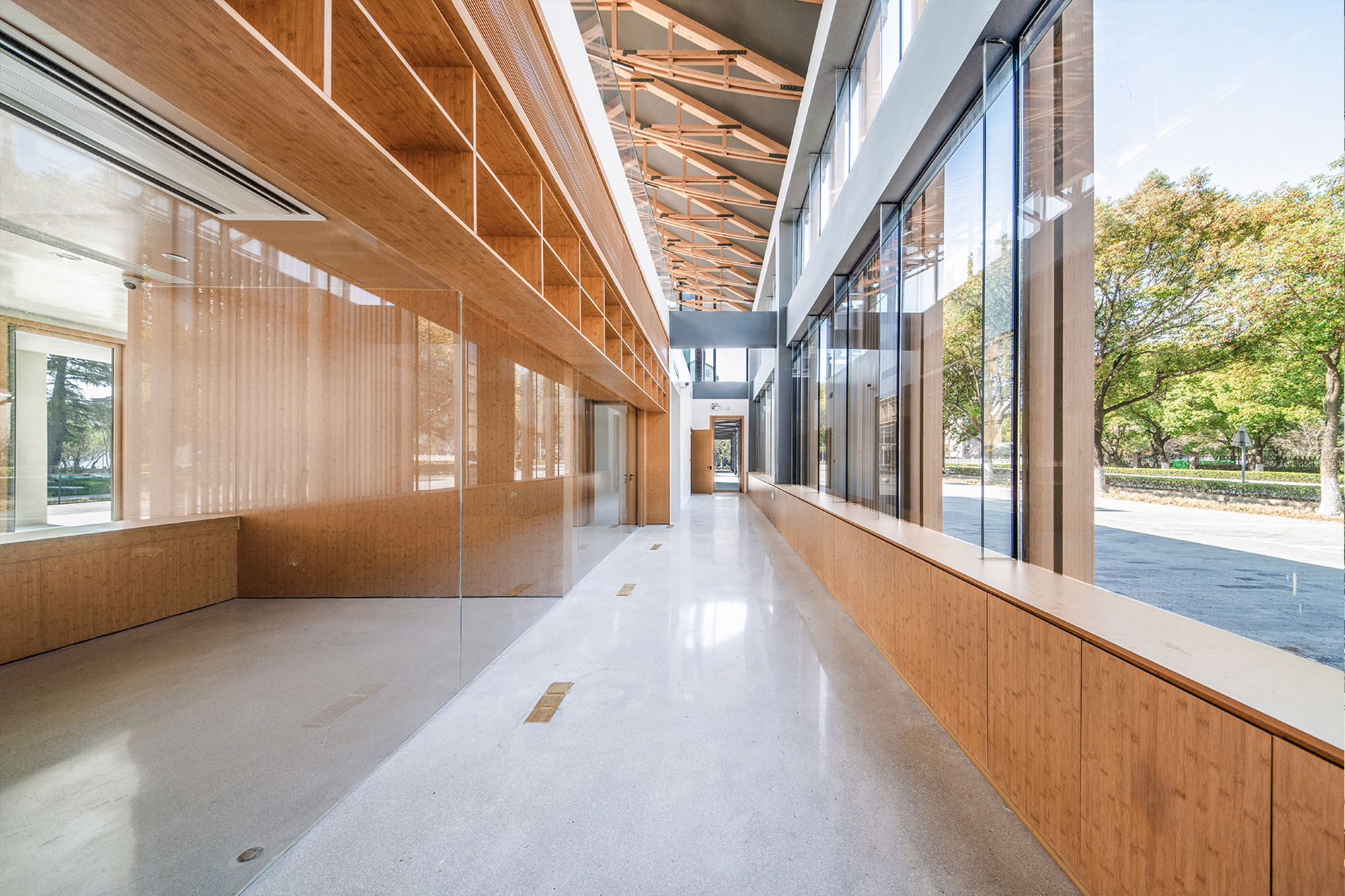 Corridor with timber-clad walls beneath exposed truss ceiling and continuous clerestory windows on both sides