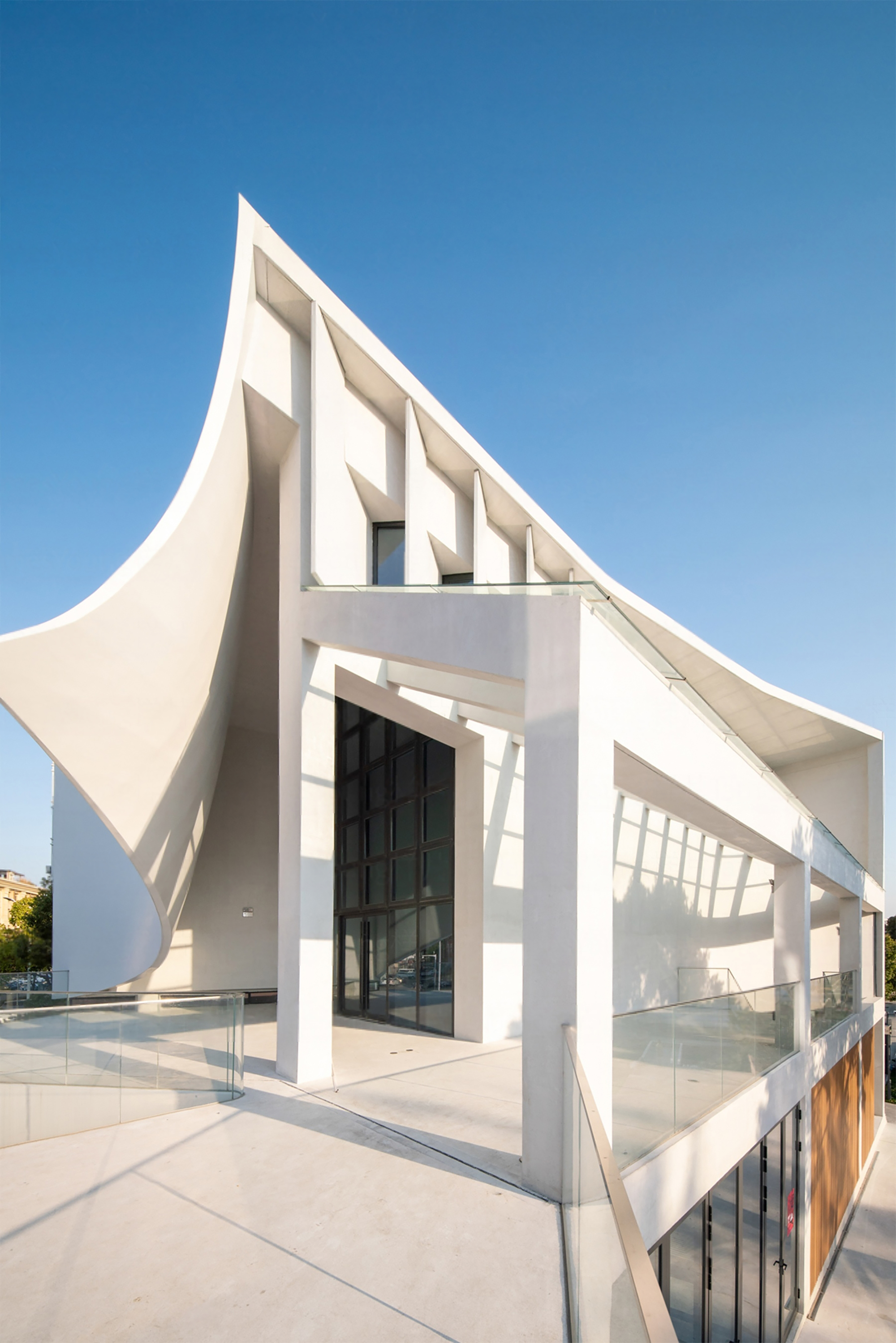 White faceted facade with deep window recesses and a triangular roofline under clear blue sky