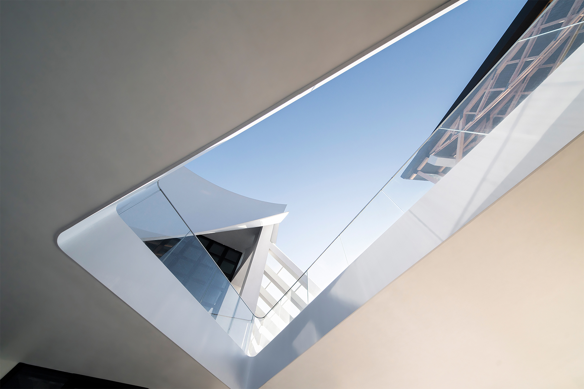 View upward through an angular courtyard opening framed by white walls and exposed steel structure