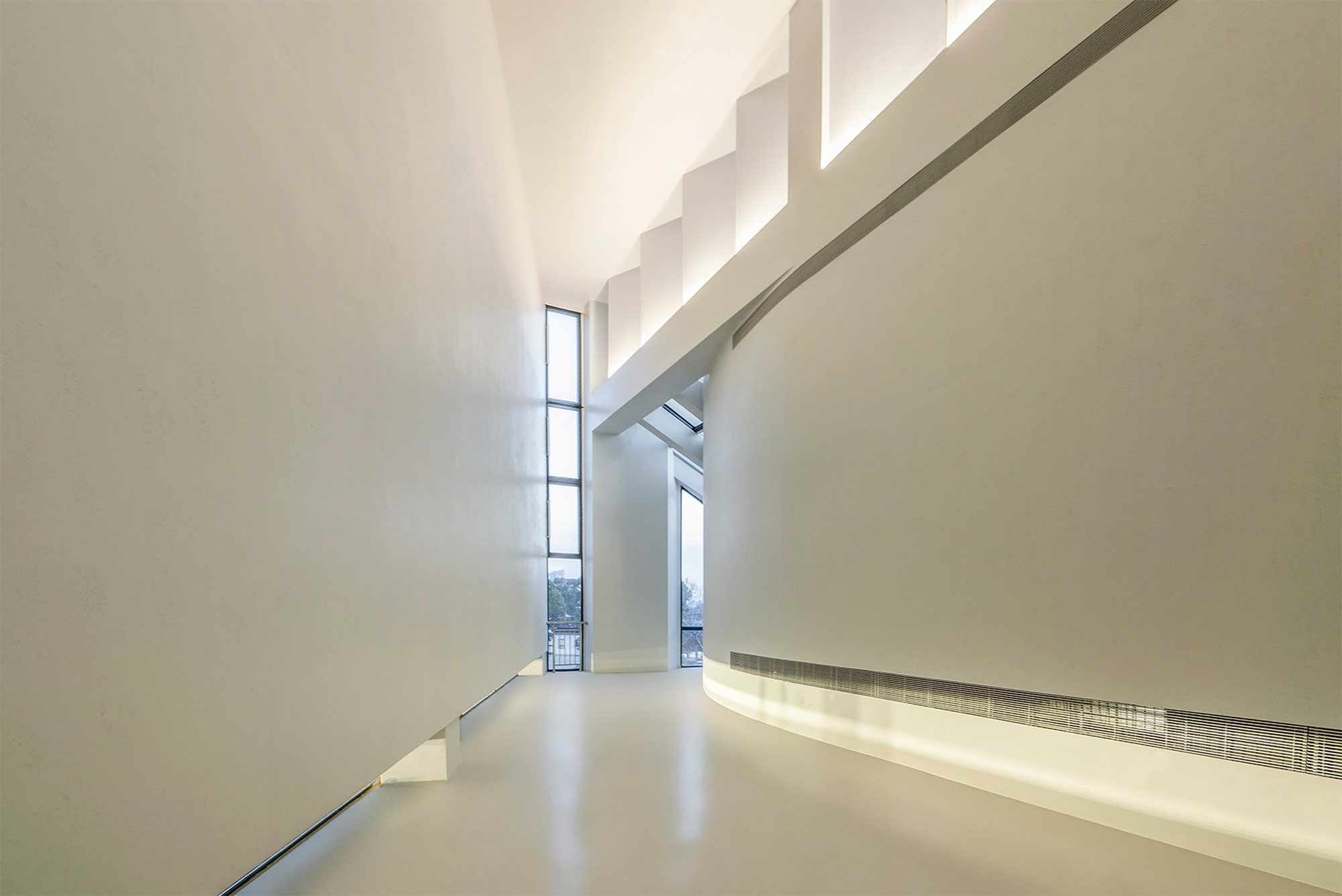 Gallery corridor with white polished floor and recessed linear ceiling lighting along the wall