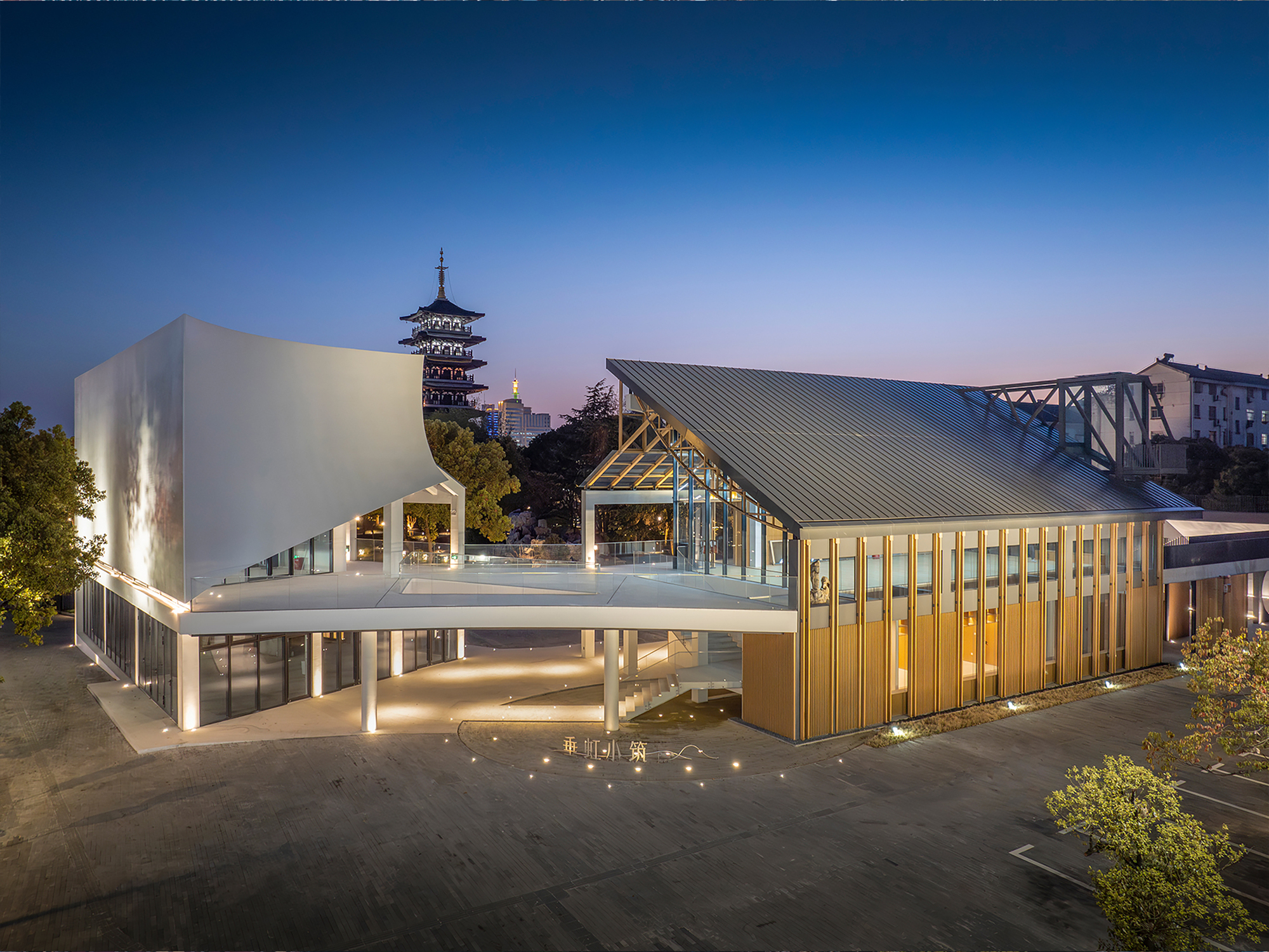 Twilight view of the illuminated volumes with corrugated metal roof and exposed timber truss structure