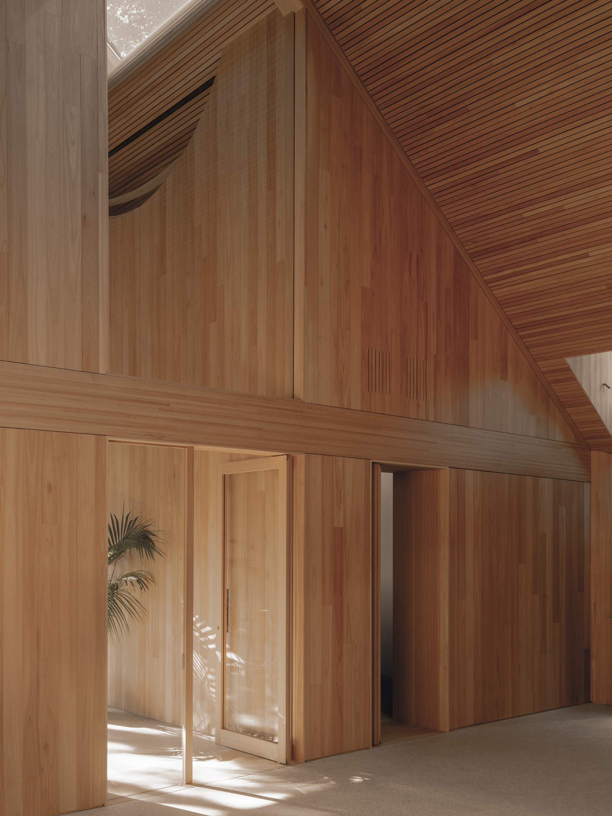 Interior view of timber-clad walls meeting sloped slatted ceiling with glazed doors facing a courtyard