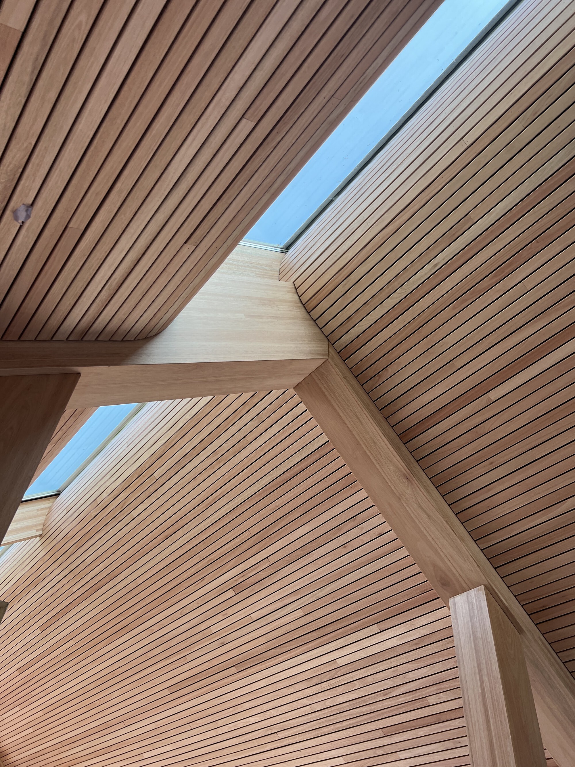Slatted timber ceiling planes meeting at angles with narrow skylight running between them