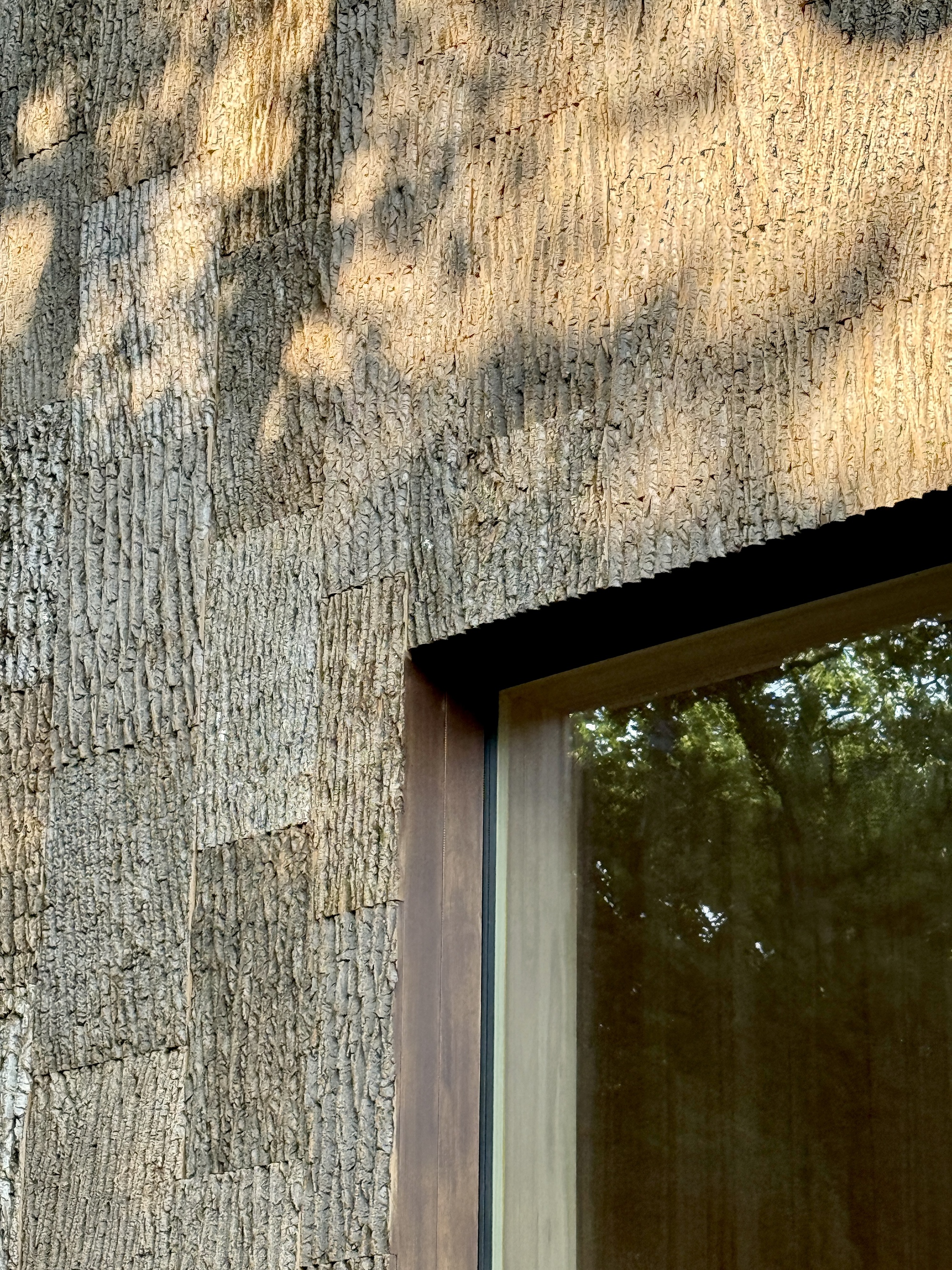 Textured tree bark cladding on the exterior wall beside a recessed window in afternoon sun