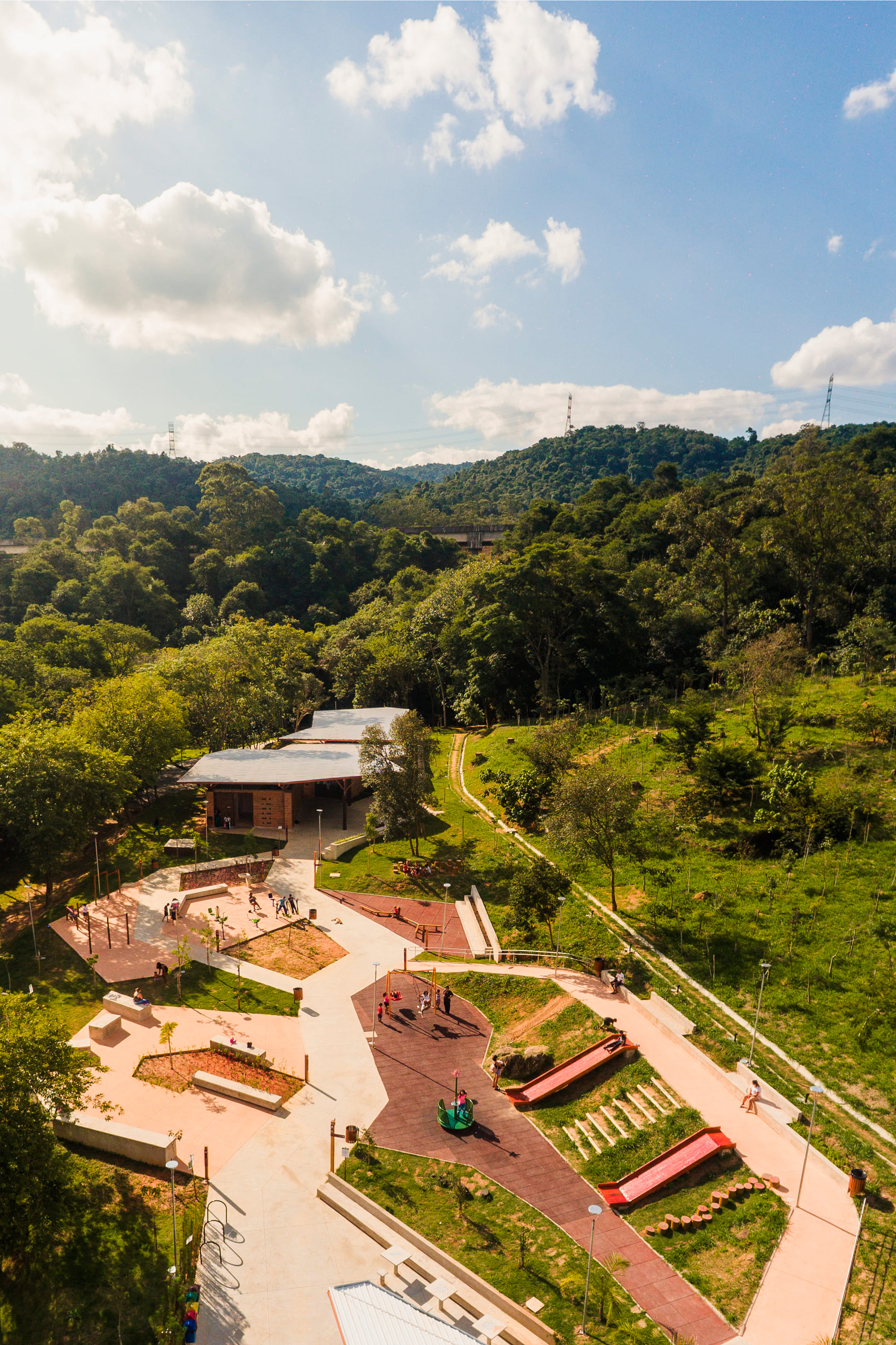 Aerial view of the playground and low-slung pavilion nestled in a forested valley below rolling hills