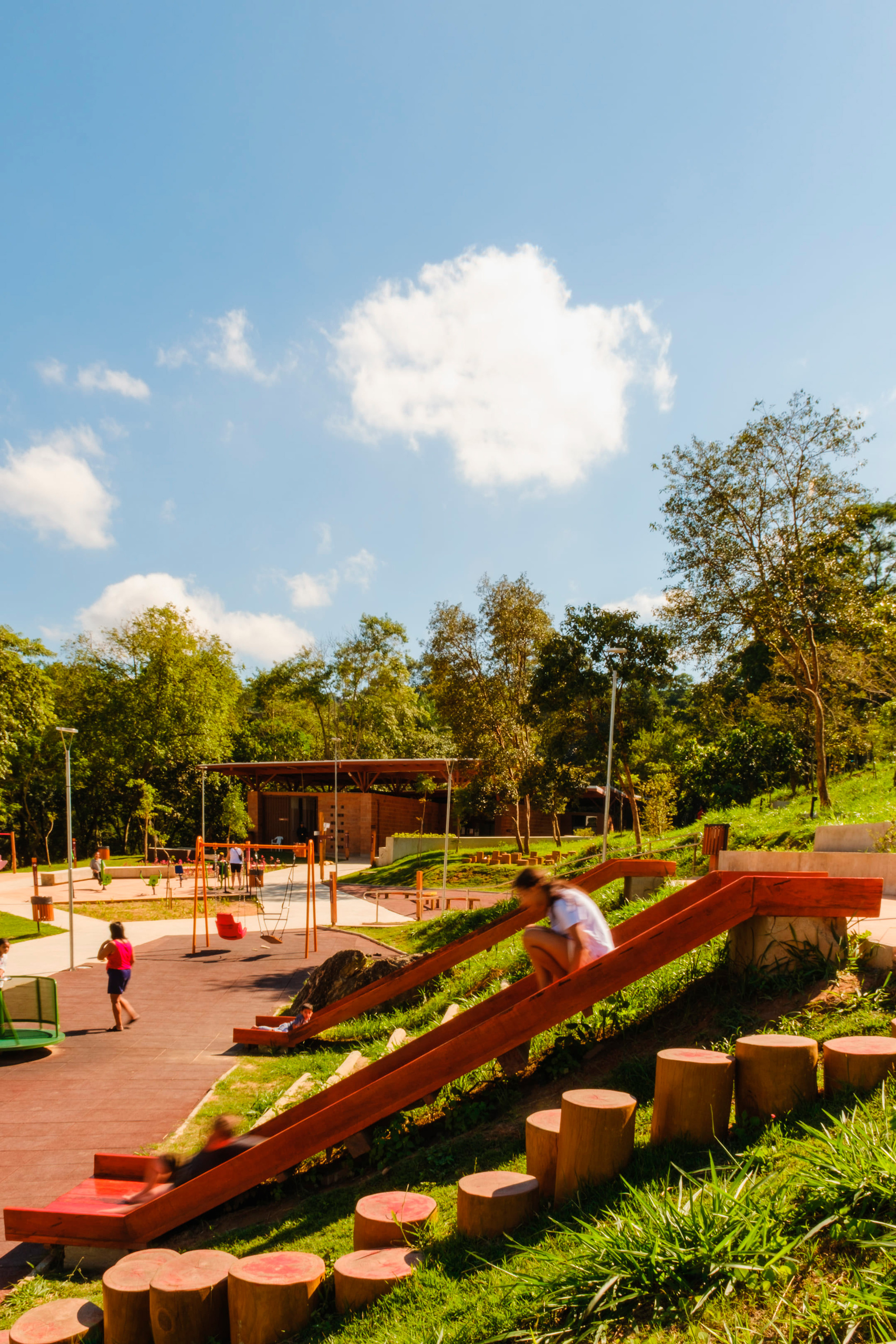 Terraced play area with angled timber ramps and cylindrical log seating under scattered clouds