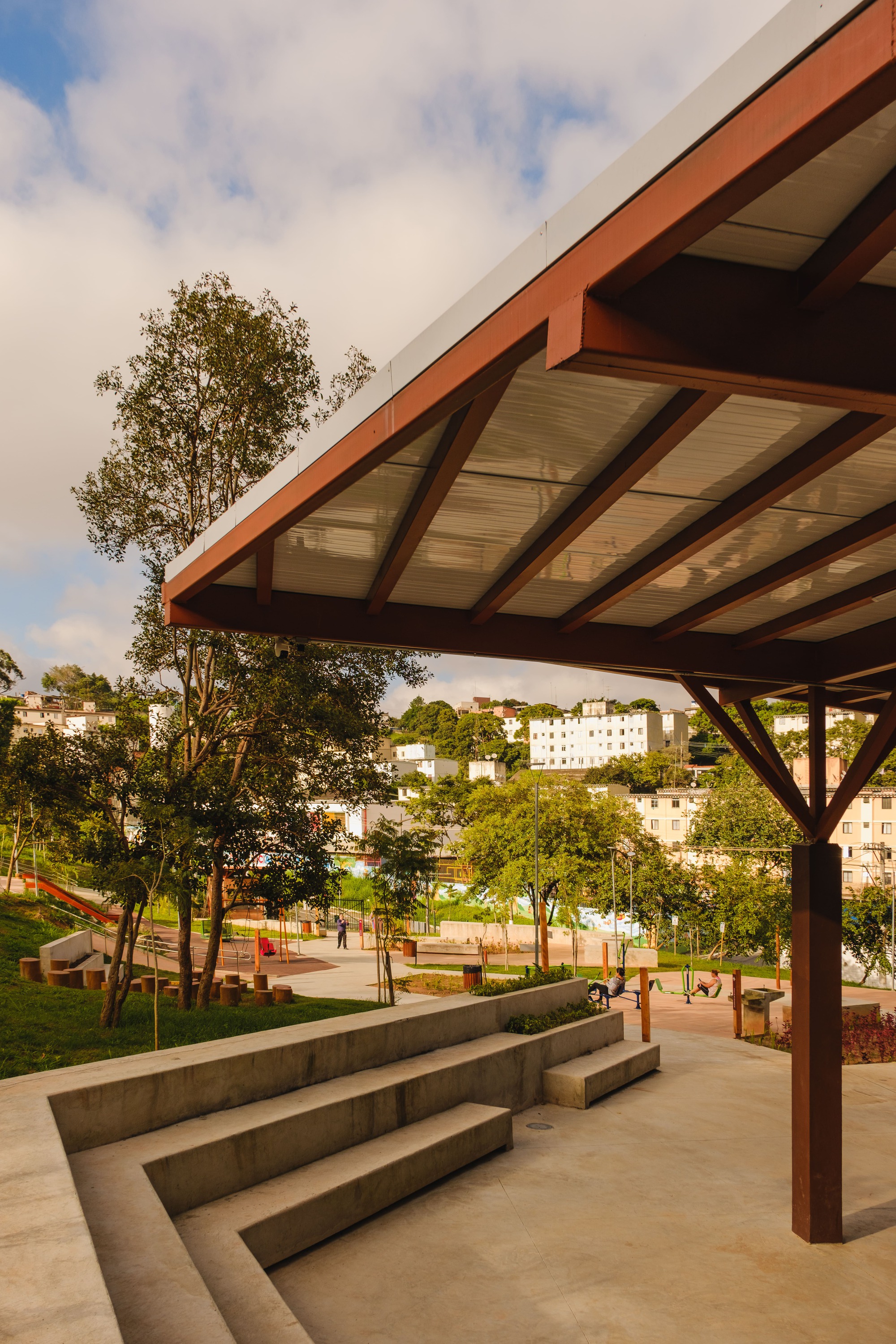 Cantilevered roof canopy with exposed timber structure above concrete steps and playground beyond