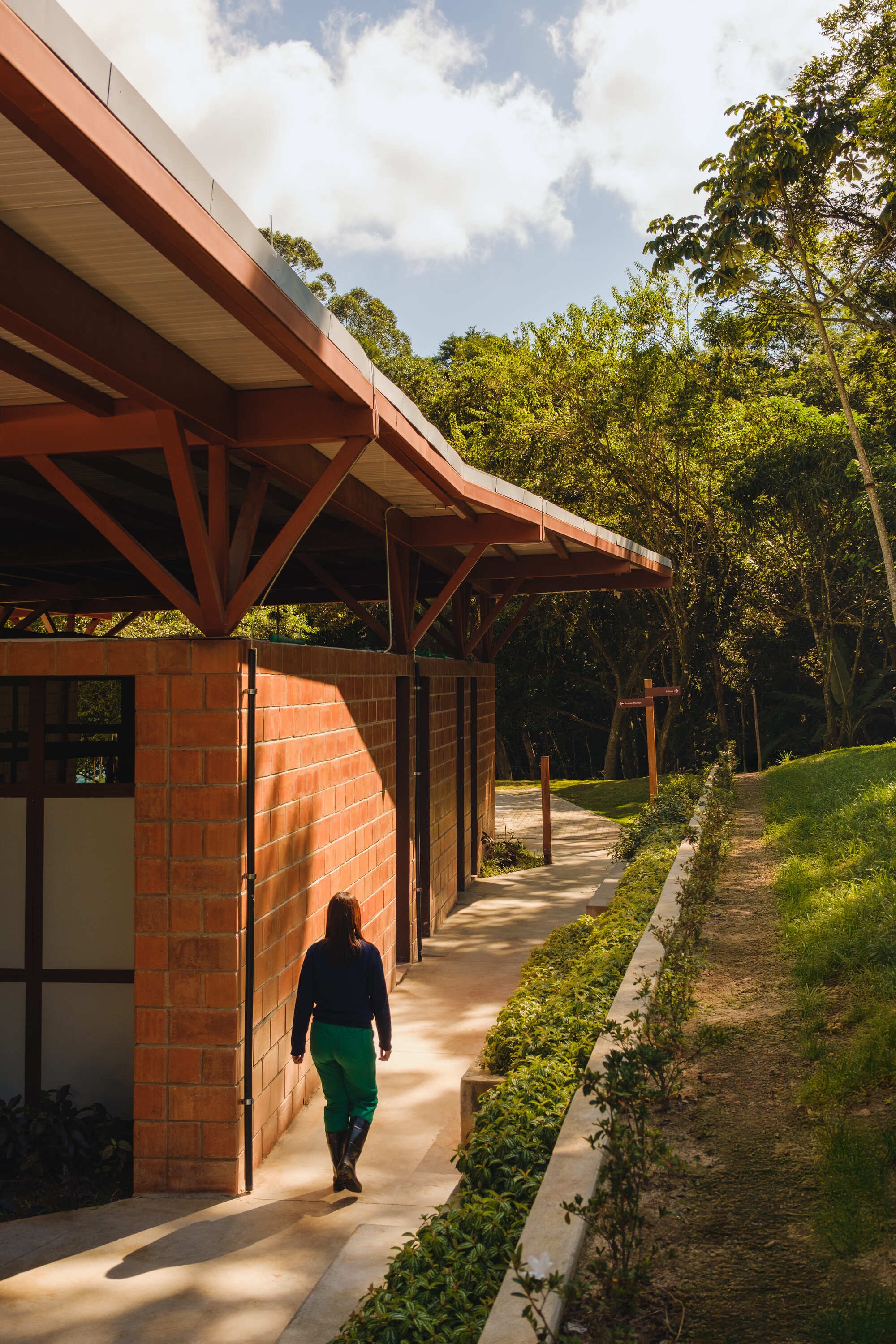 Covered walkway with exposed timber beams and red brick walls as a person walks through dappled afternoon light
