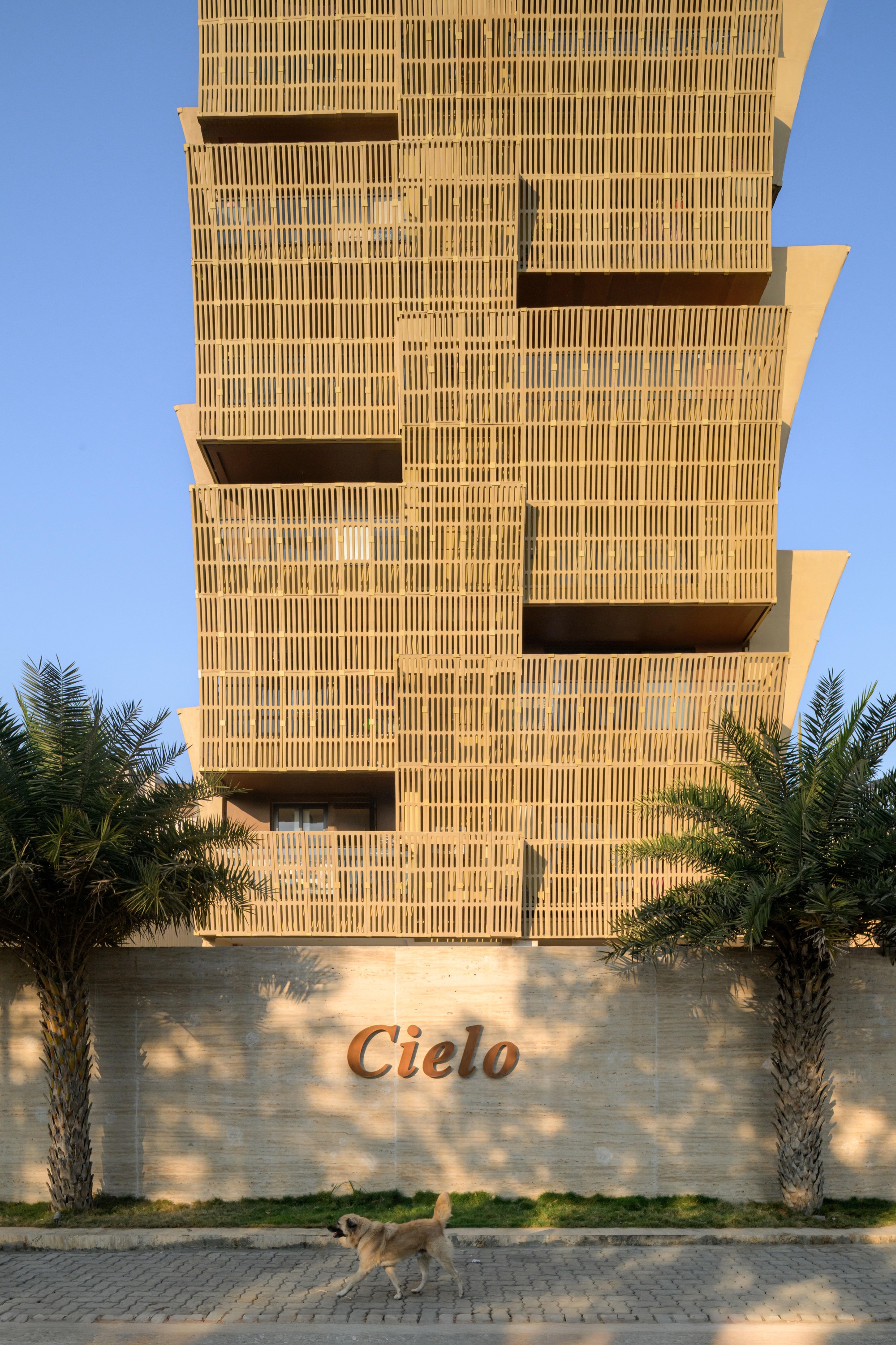 Tower entrance with vertical brick screen above a low boundary wall and flanking palm trees