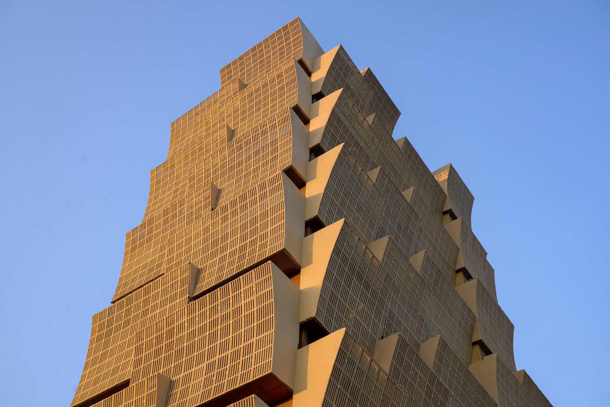Upward view of the stepped tower facade with ribbed brick and deep recessed balconies against a clear sky