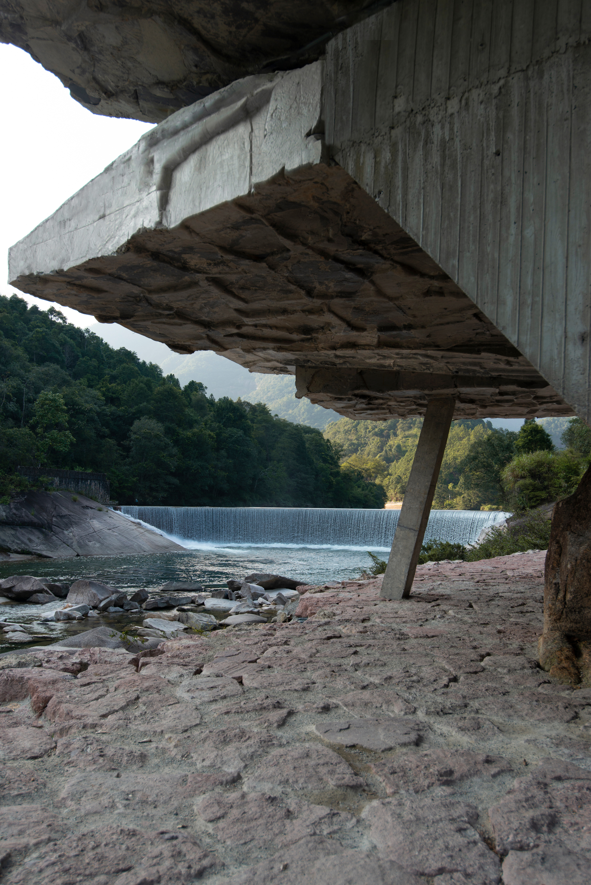 Underside of the cantilevered concrete slab showing board-formed texture and stone strata above the river