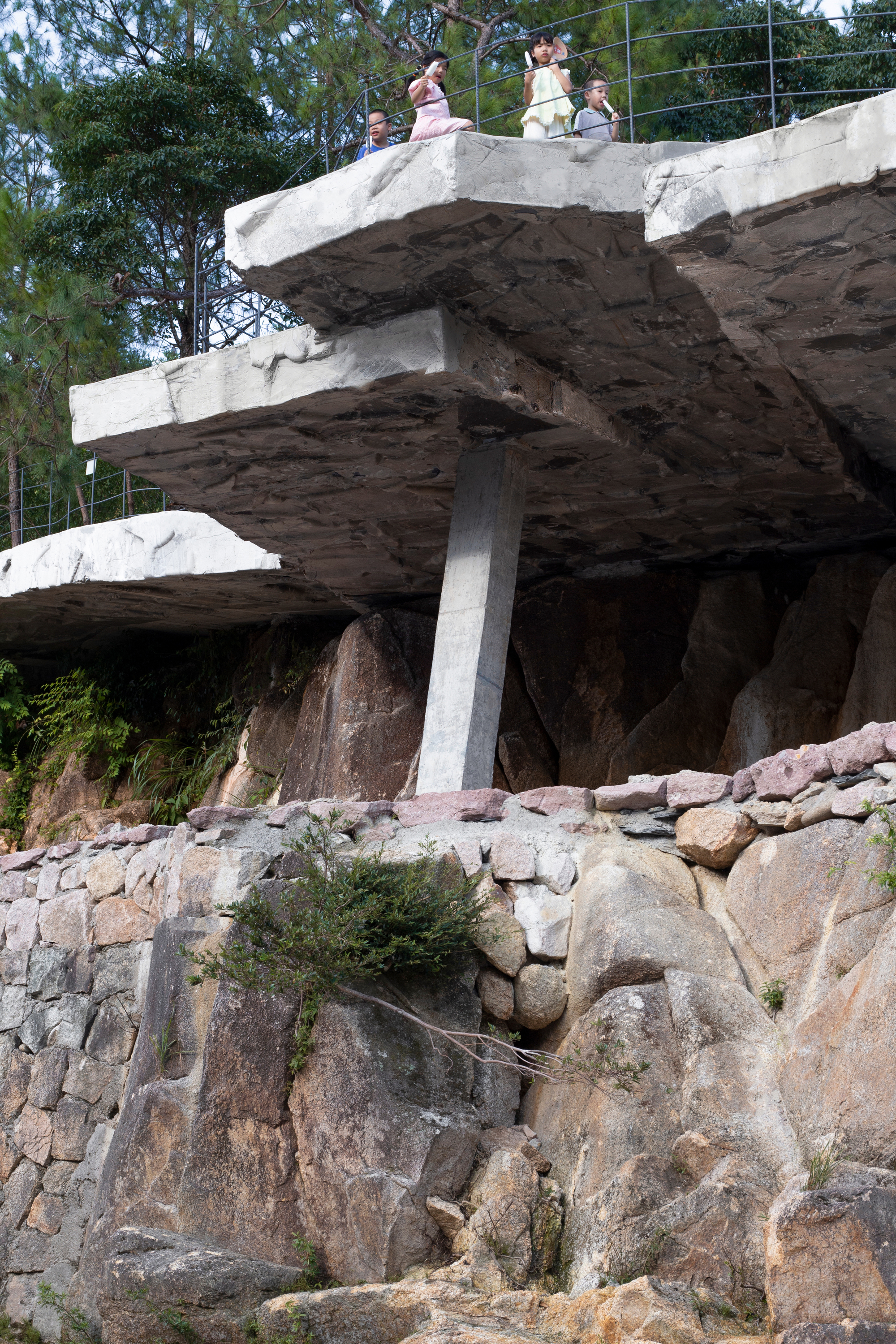 Angled view of cantilevered concrete platforms on stone pillar with visitors above and boulders below
