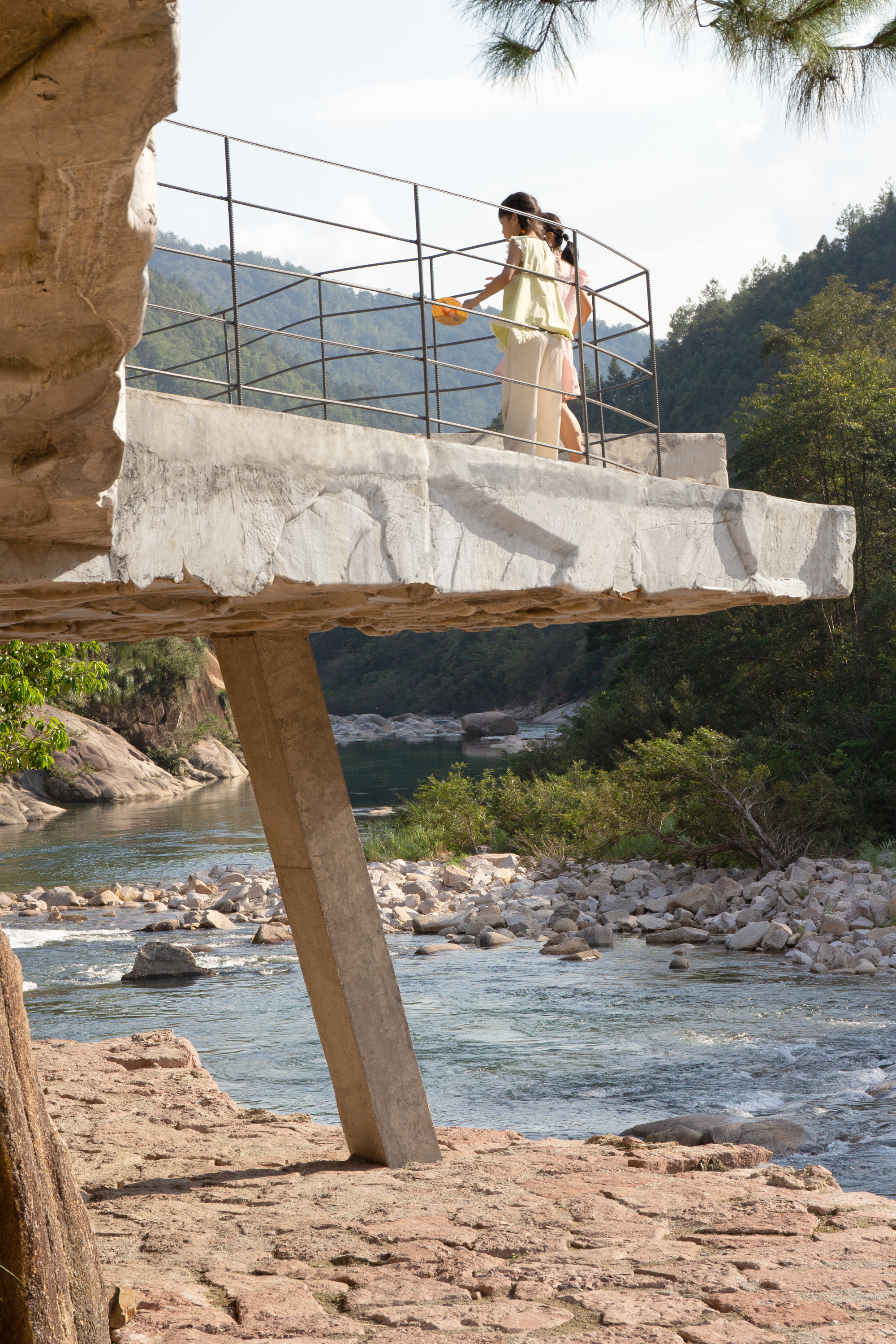 Concrete observation deck with wire railing supported by single column above a river