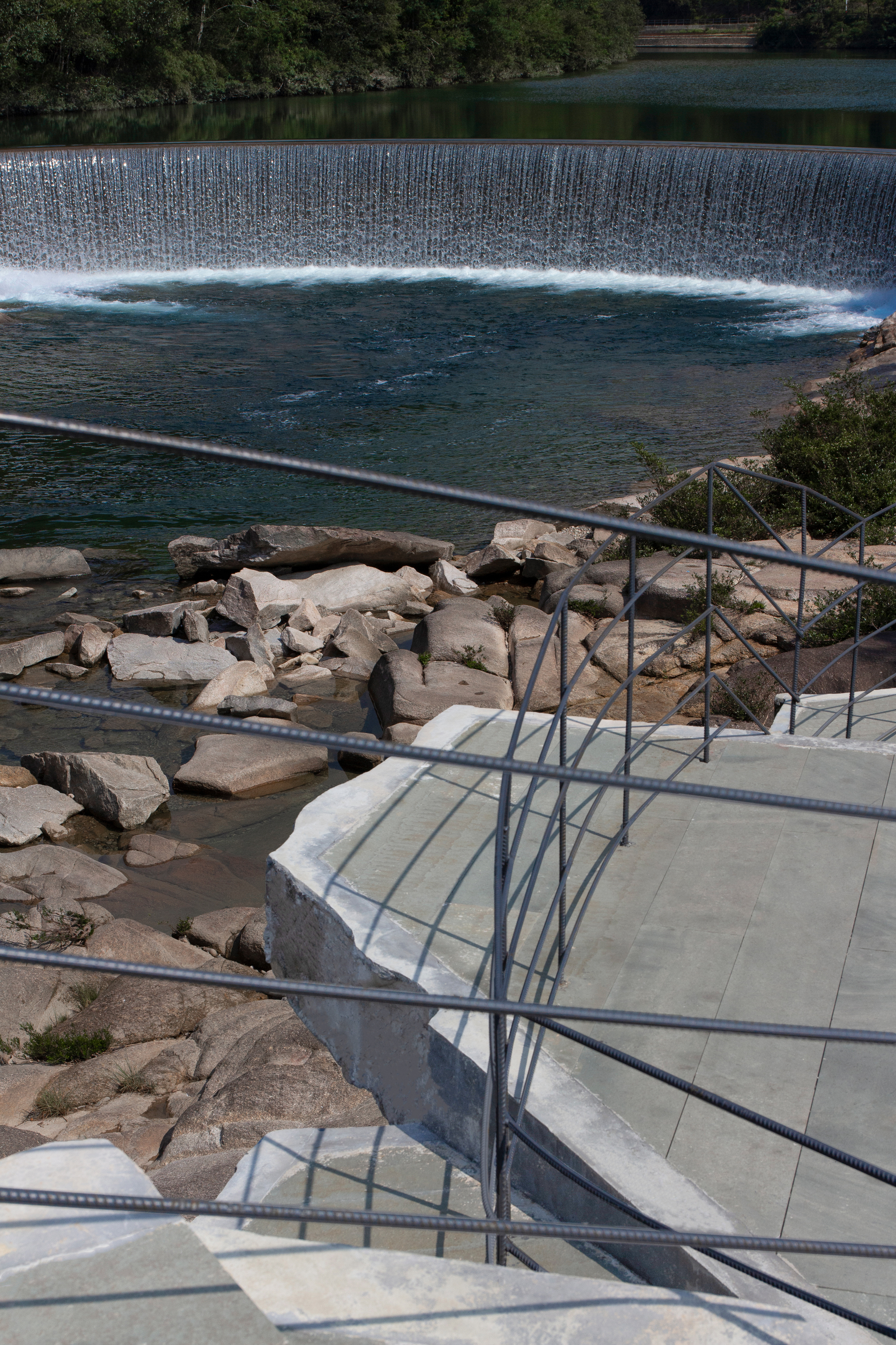 Concrete stairway with cable railing leading down to rocky ledges beside a weir flowing across dark water